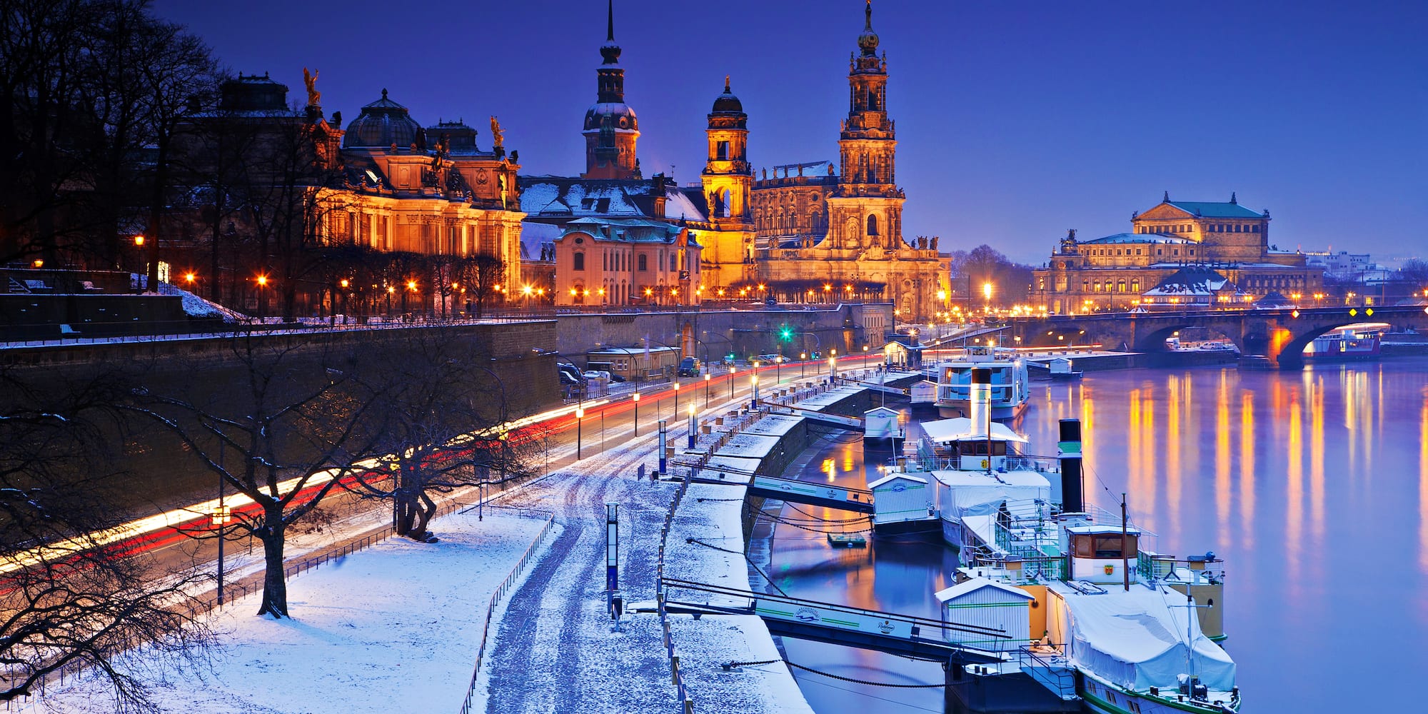 Dresden winter night: illuminated buildings, Elbe river, snow-covered bank.