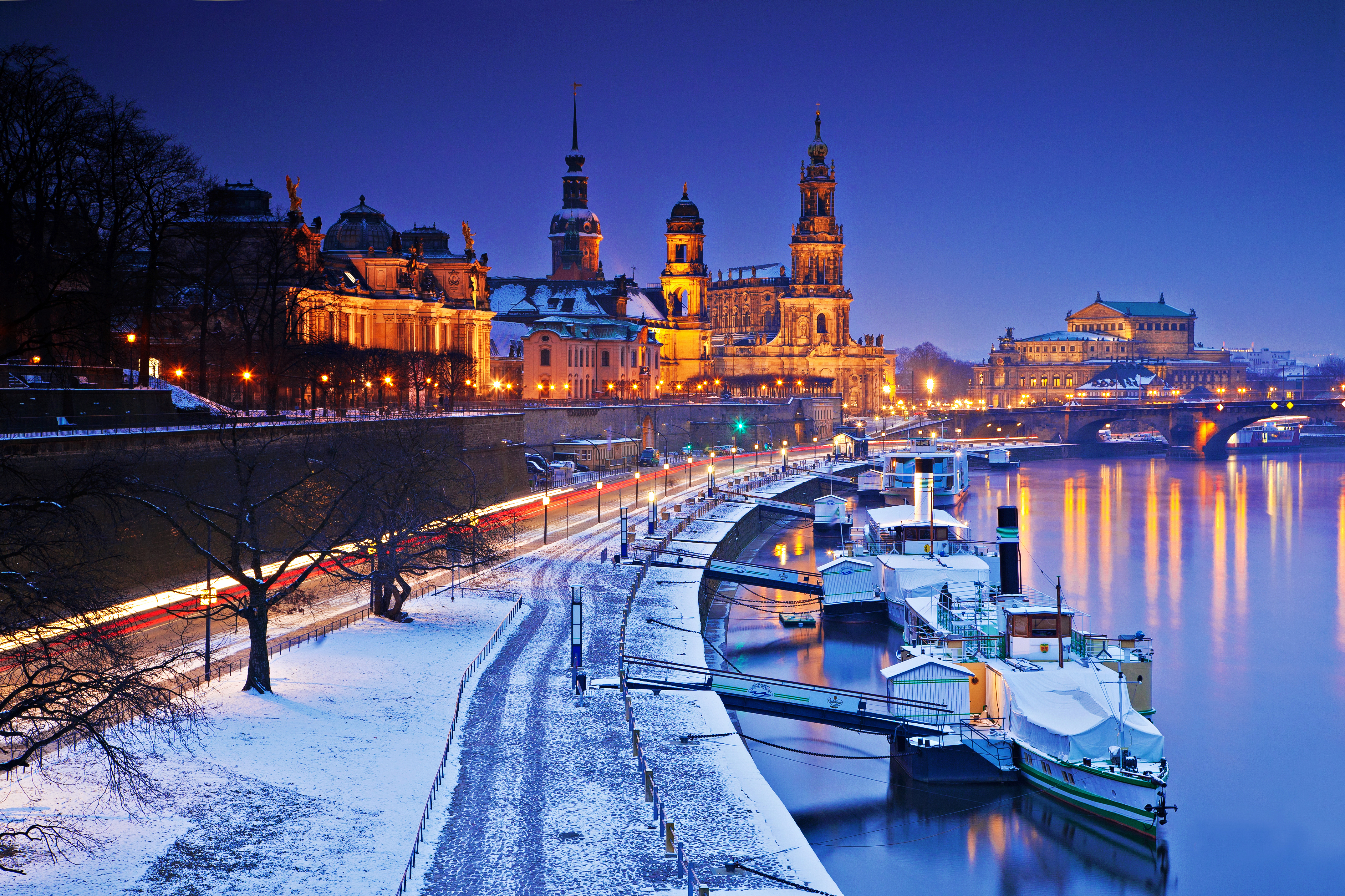Dresden winter night: illuminated buildings, Elbe river, snow-covered bank.