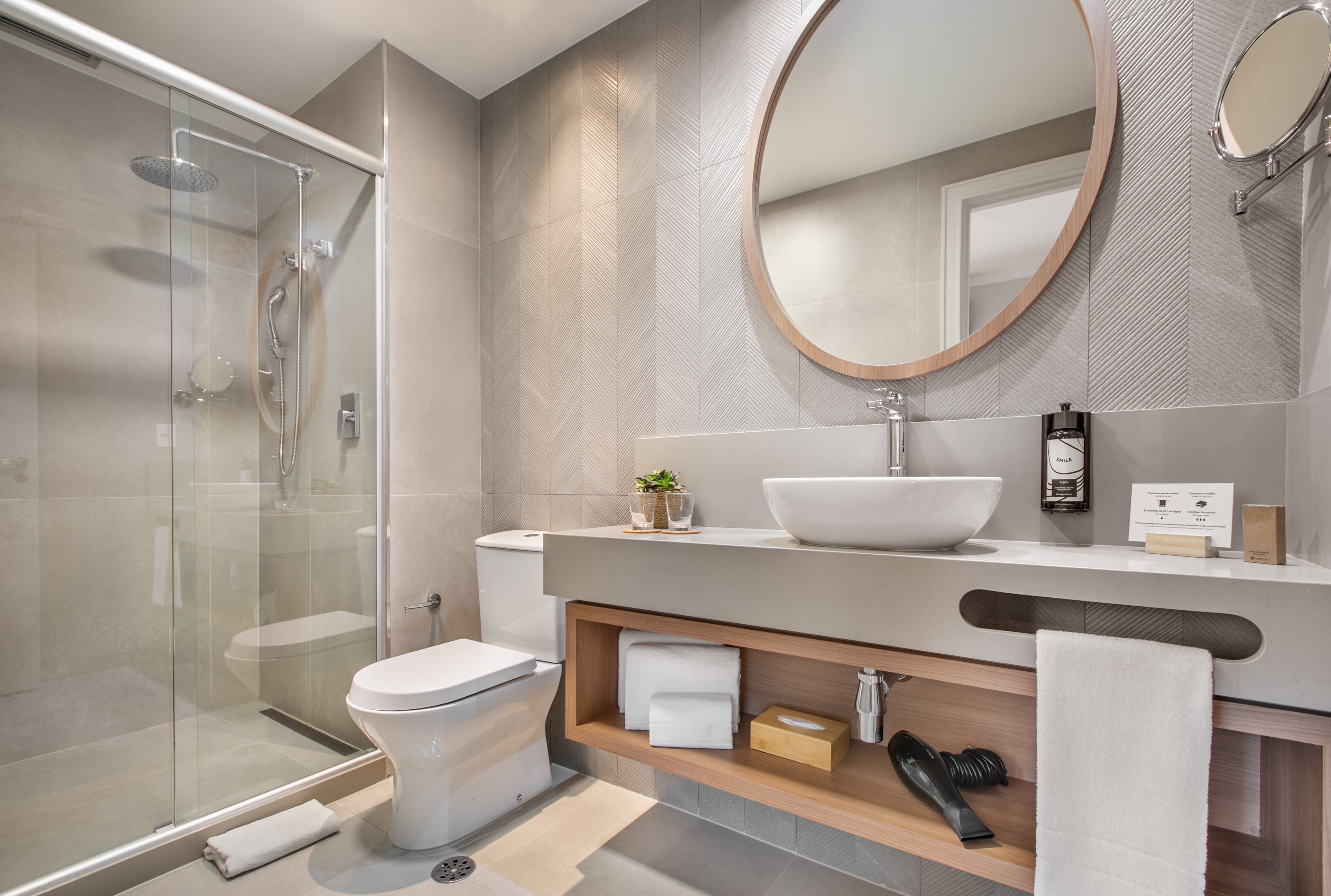 Modern hotel bathroom with glass shower, toilet, vanity, and round mirror.