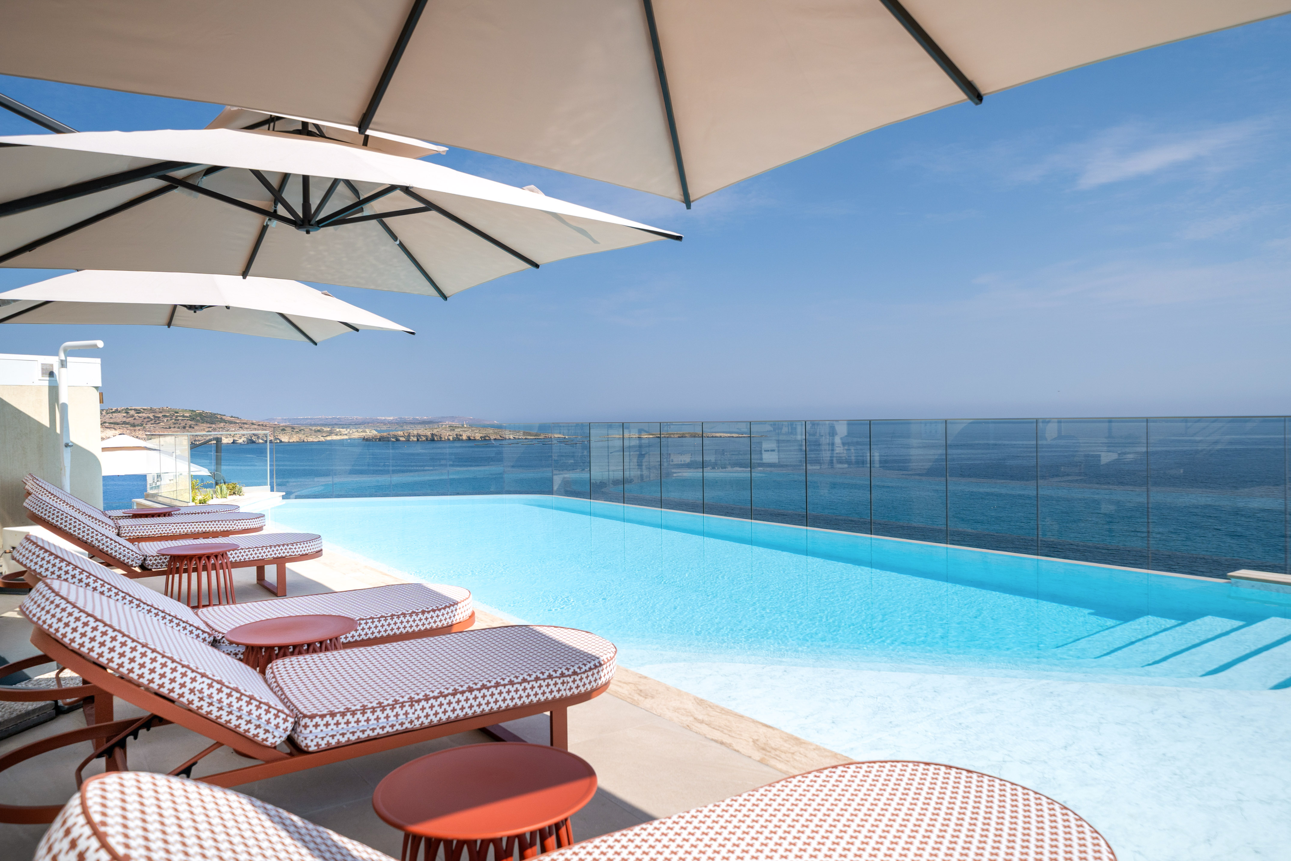 Luxury resort infinity pool with stunning sea view, lounge chairs, umbrellas.