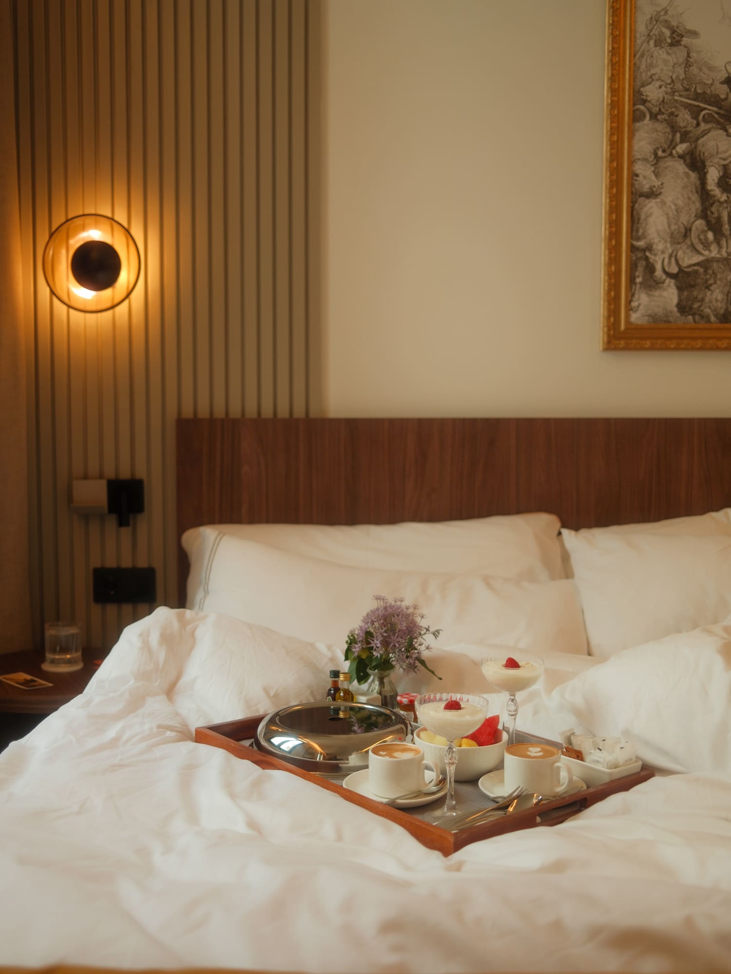 Hotel breakfast in bed: coffee, fruit, dessert, and flowers.