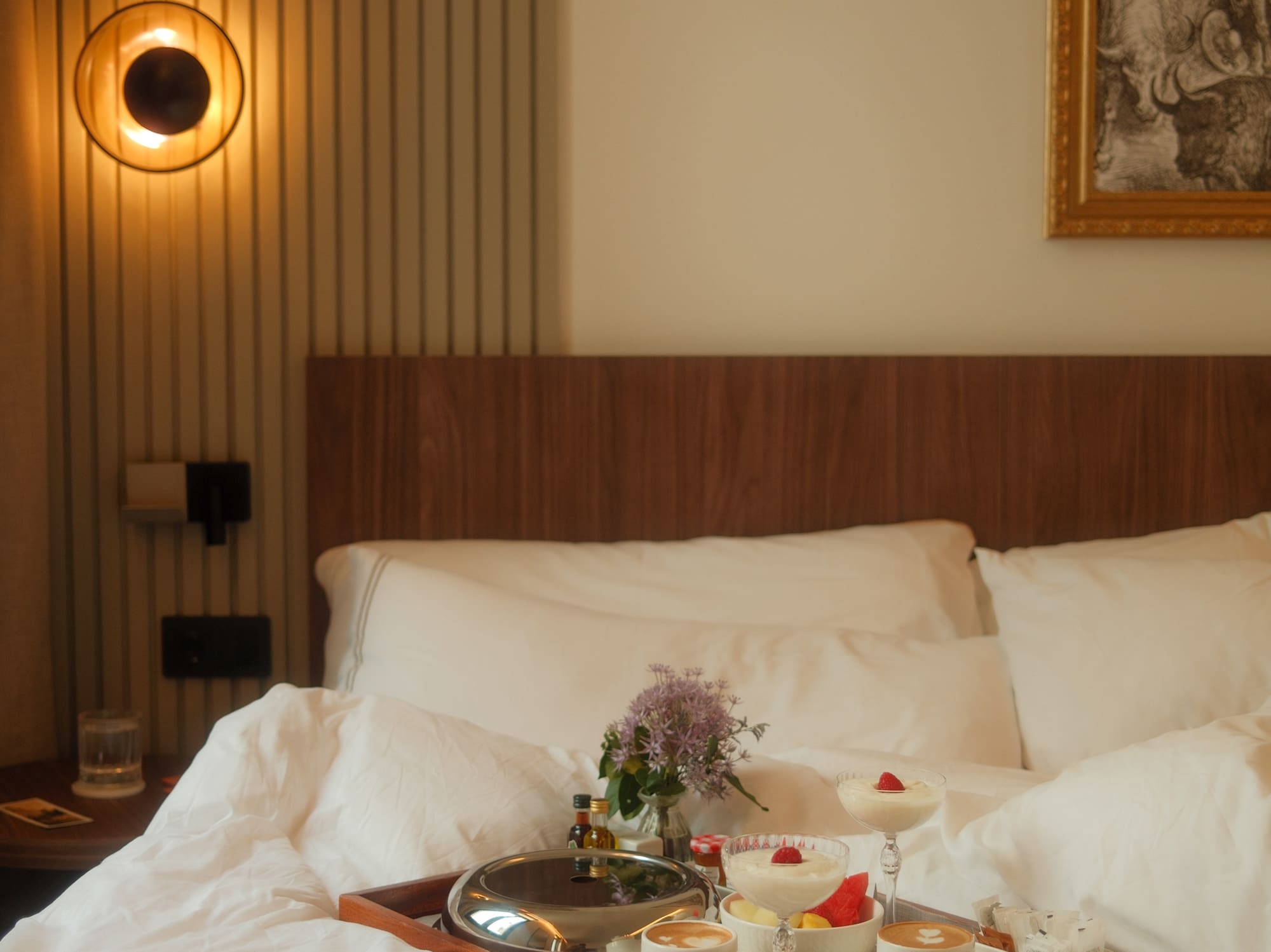 Hotel room service breakfast in bed with coffee, fruit, and flowers.