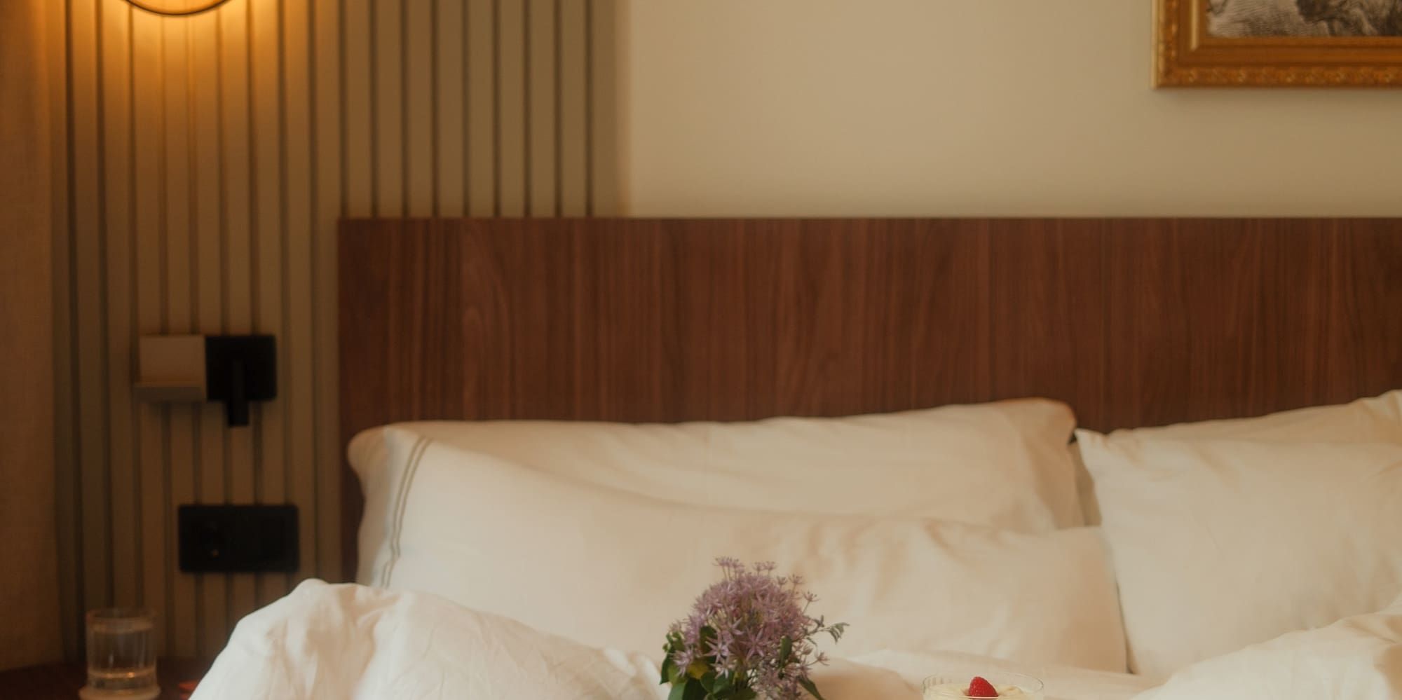 Hotel room service breakfast in bed with coffee, fruit, and flowers.