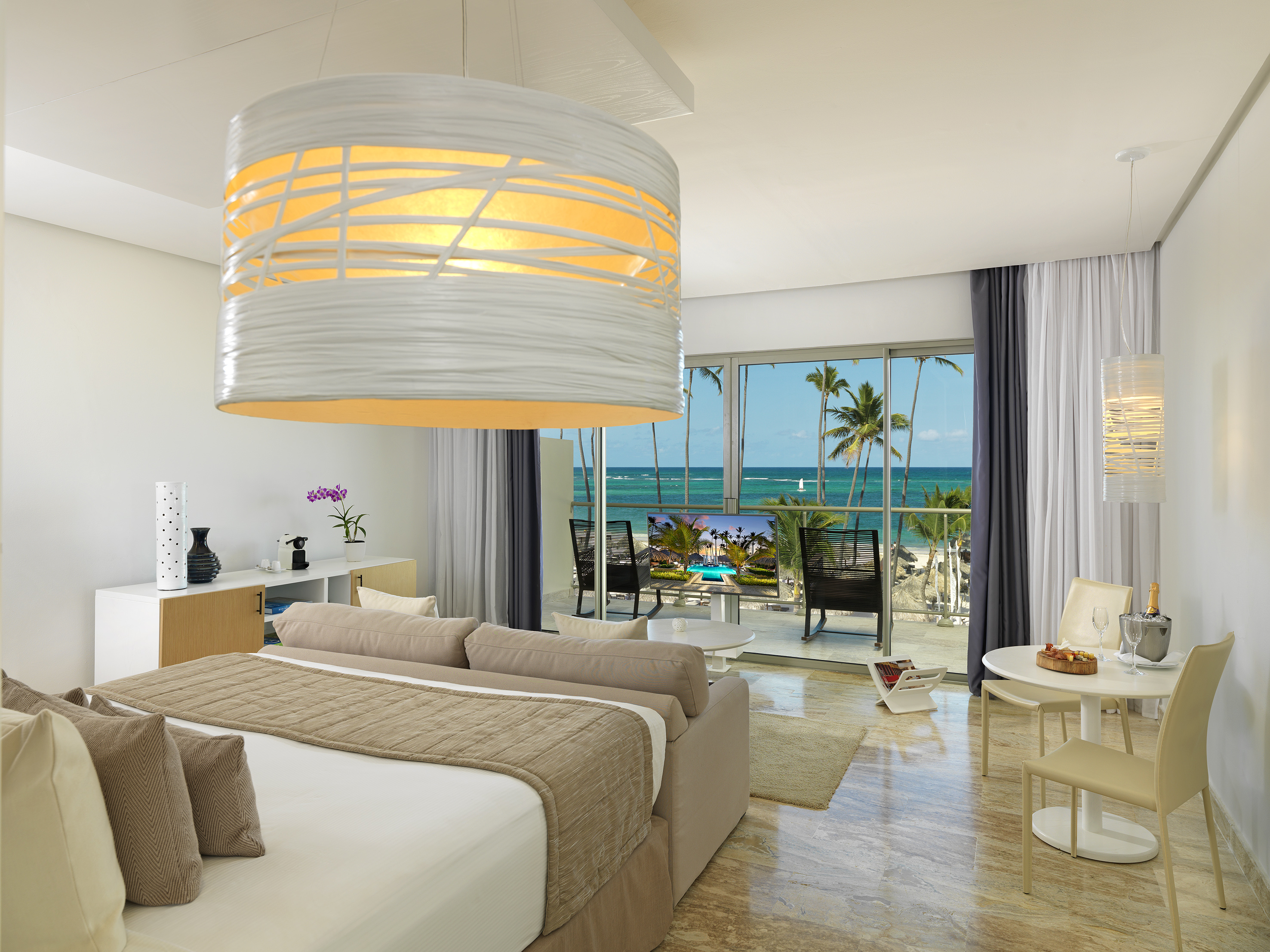 Ocean view hotel suite with bed, dining, and tropical beach balcony.