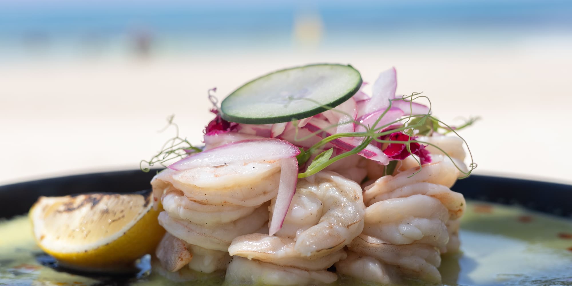 Fresh shrimp ceviche with red onion, lemon, and cucumber slice by the beach.
