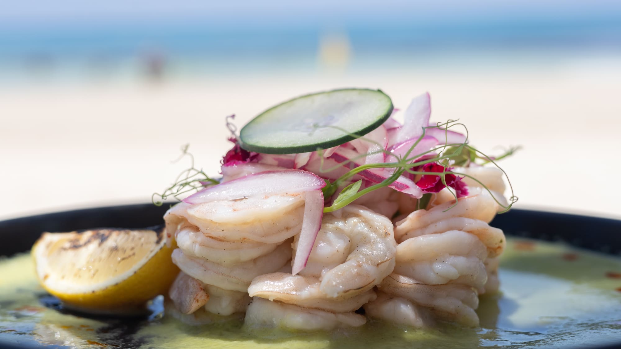 Fresh shrimp ceviche with red onion, lemon, and cucumber slice by the beach.