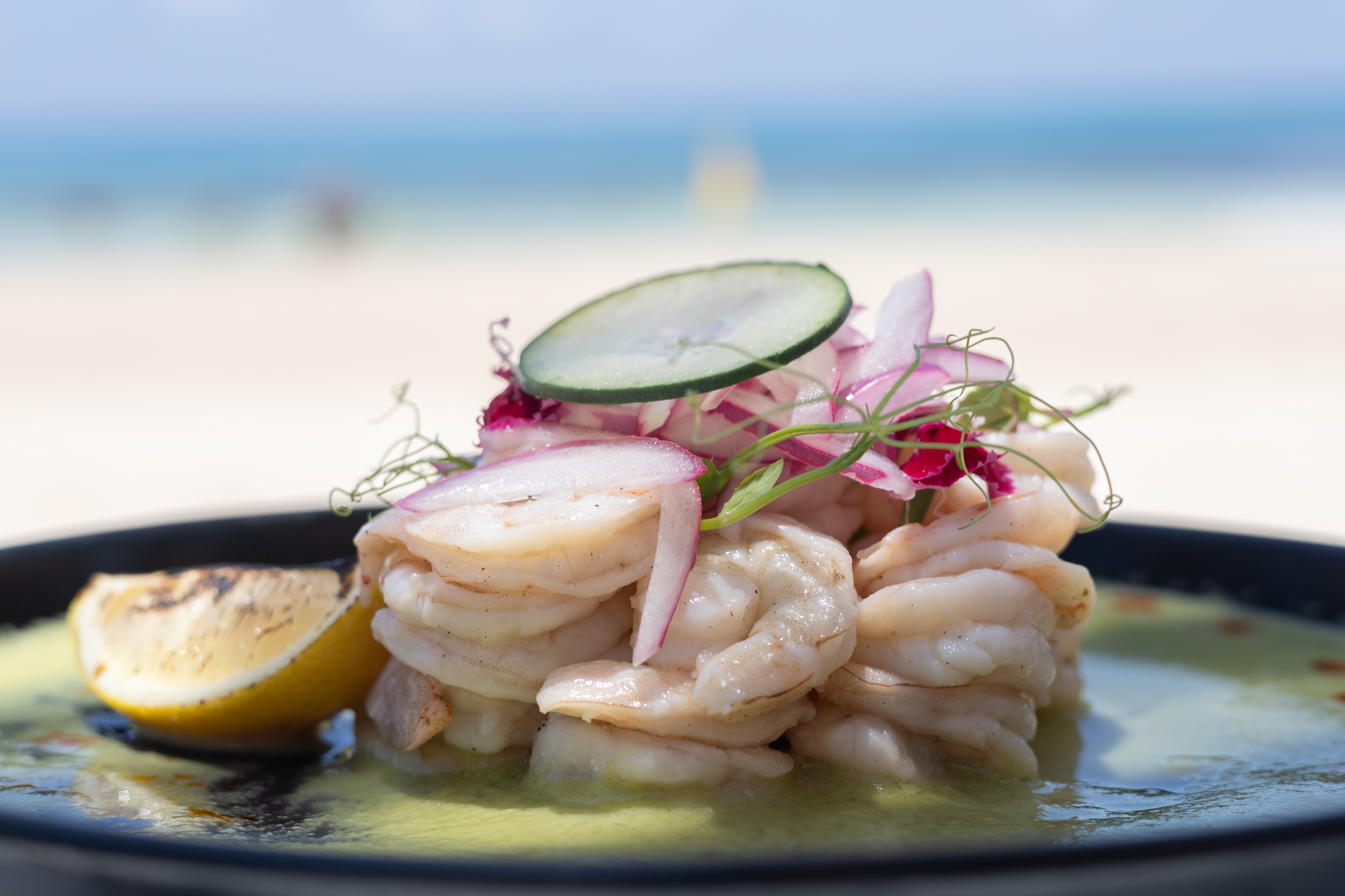Fresh shrimp ceviche with red onion, lemon, and cucumber slice by the beach.