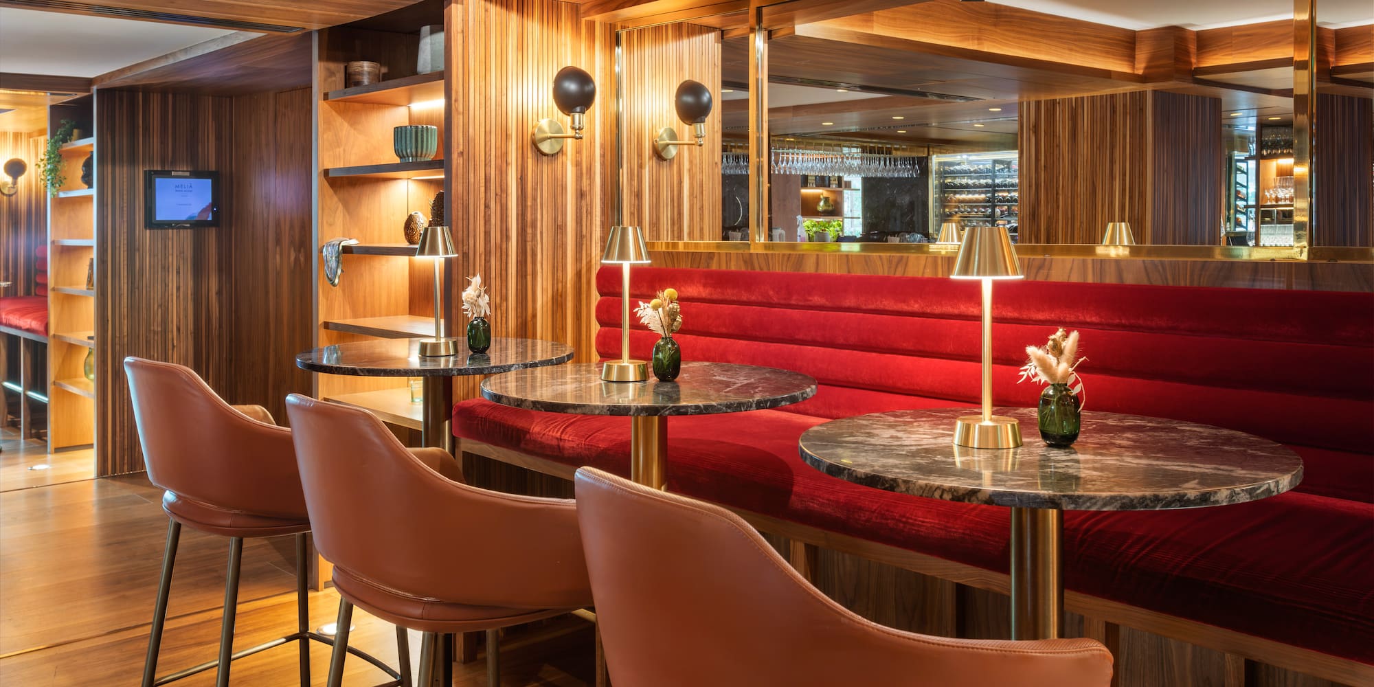 Luxurious hotel bar with red velvet seating, marble tables, and wood paneling.