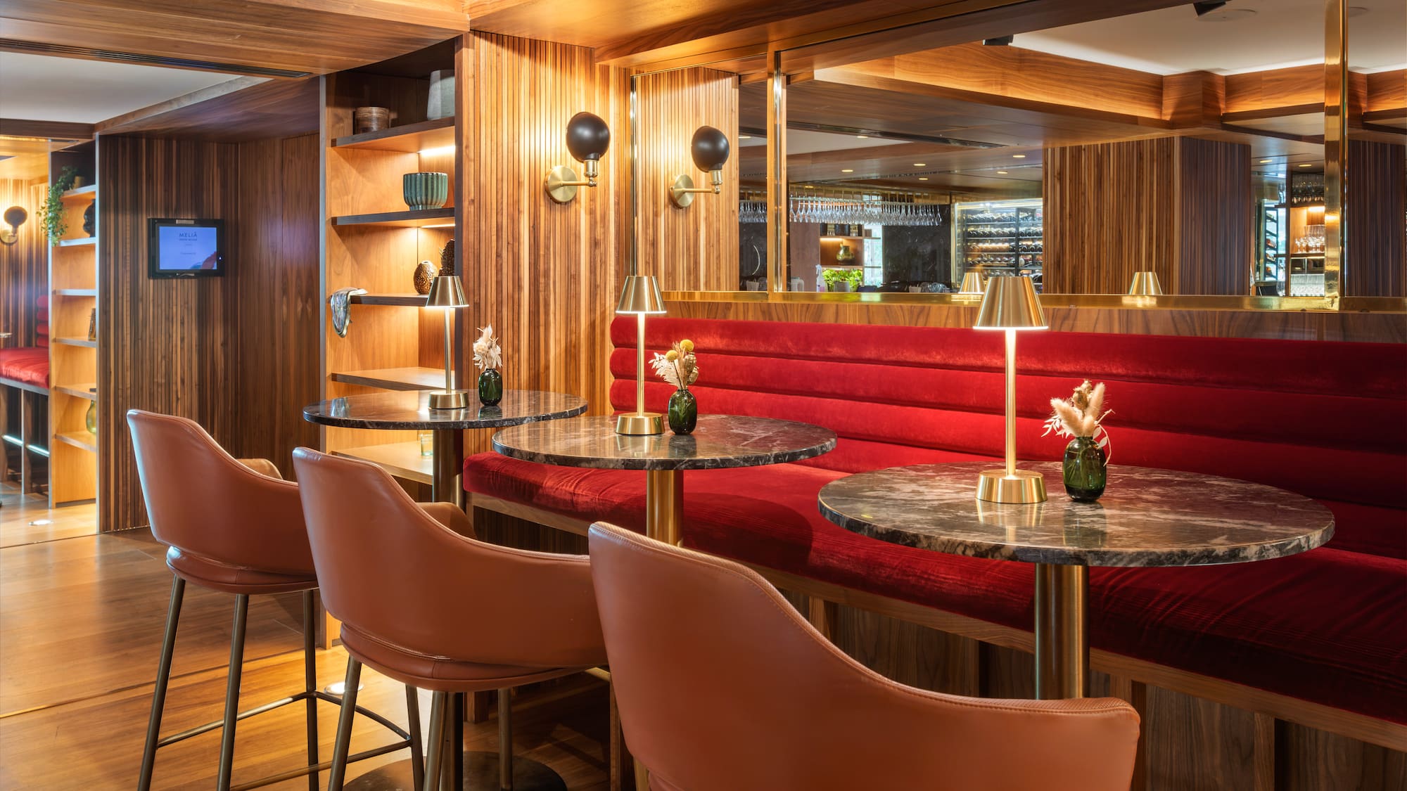 Luxurious hotel bar with red velvet seating, marble tables, and wood paneling.