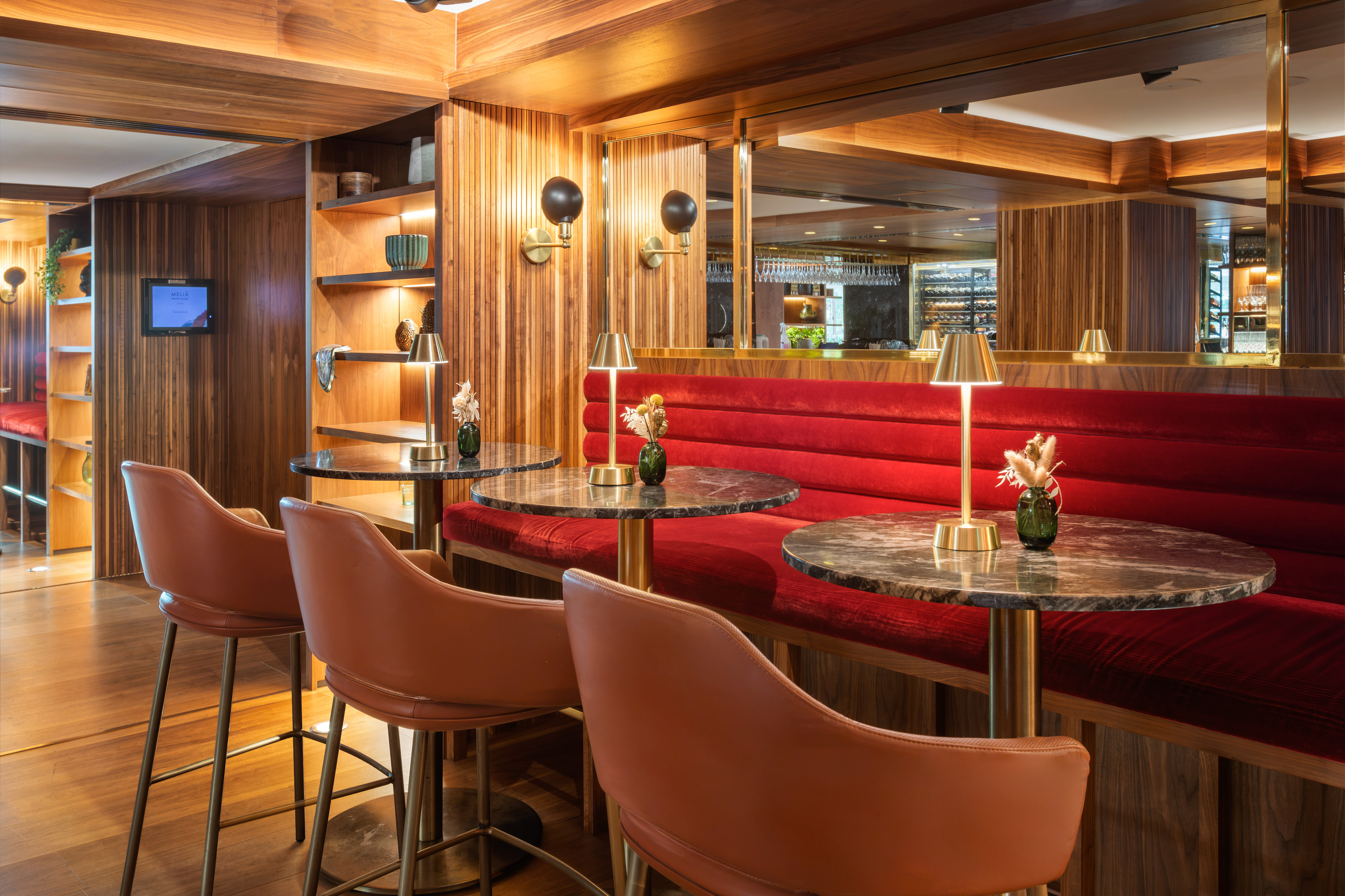 Luxurious hotel bar with red velvet seating, marble tables, and wood paneling.