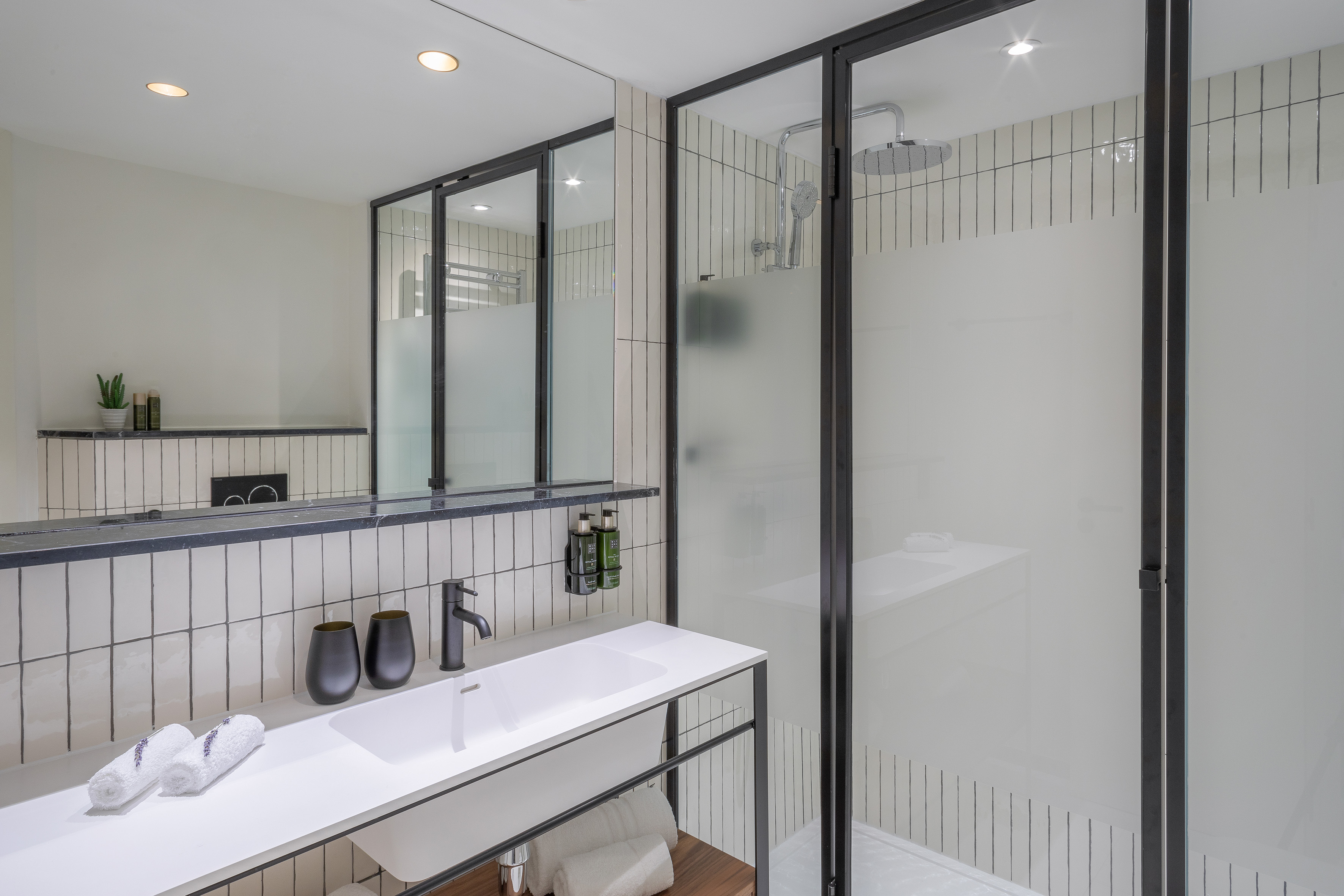 Modern bathroom with white vanity, black framed shower, and subway tile.