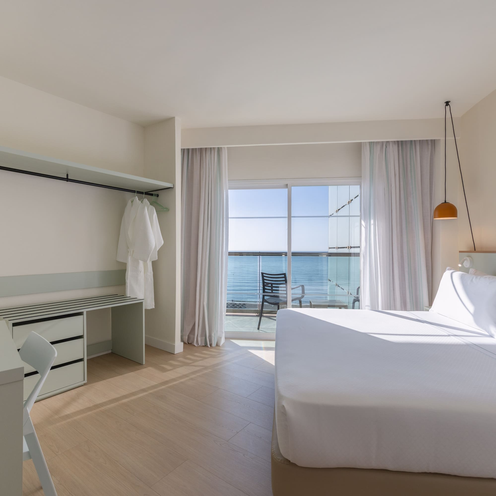 Modern hotel room with ocean view balcony, white bed, and desk.