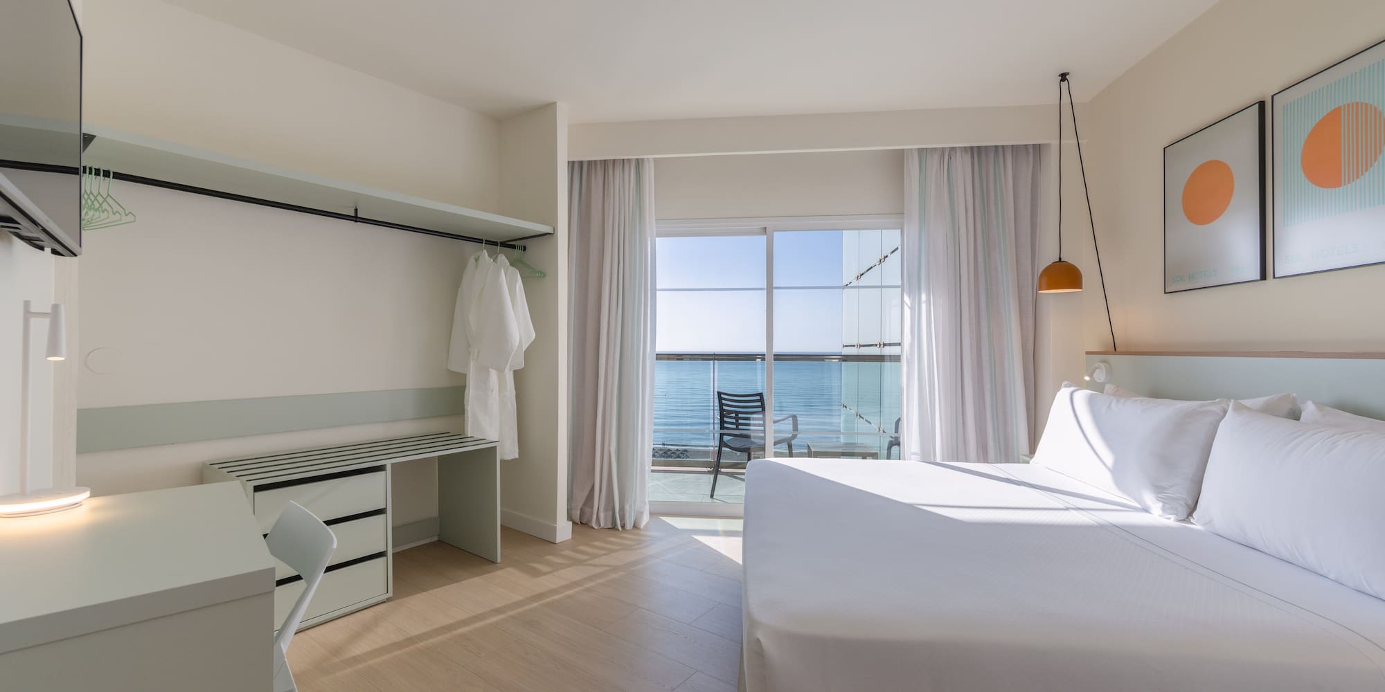 Modern hotel room with ocean view balcony, white bed, and desk.