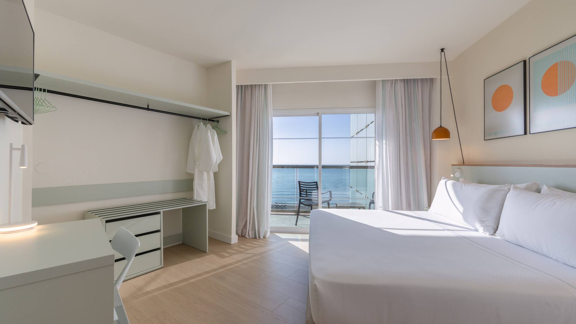Modern hotel room with ocean view balcony, white bed, and desk.