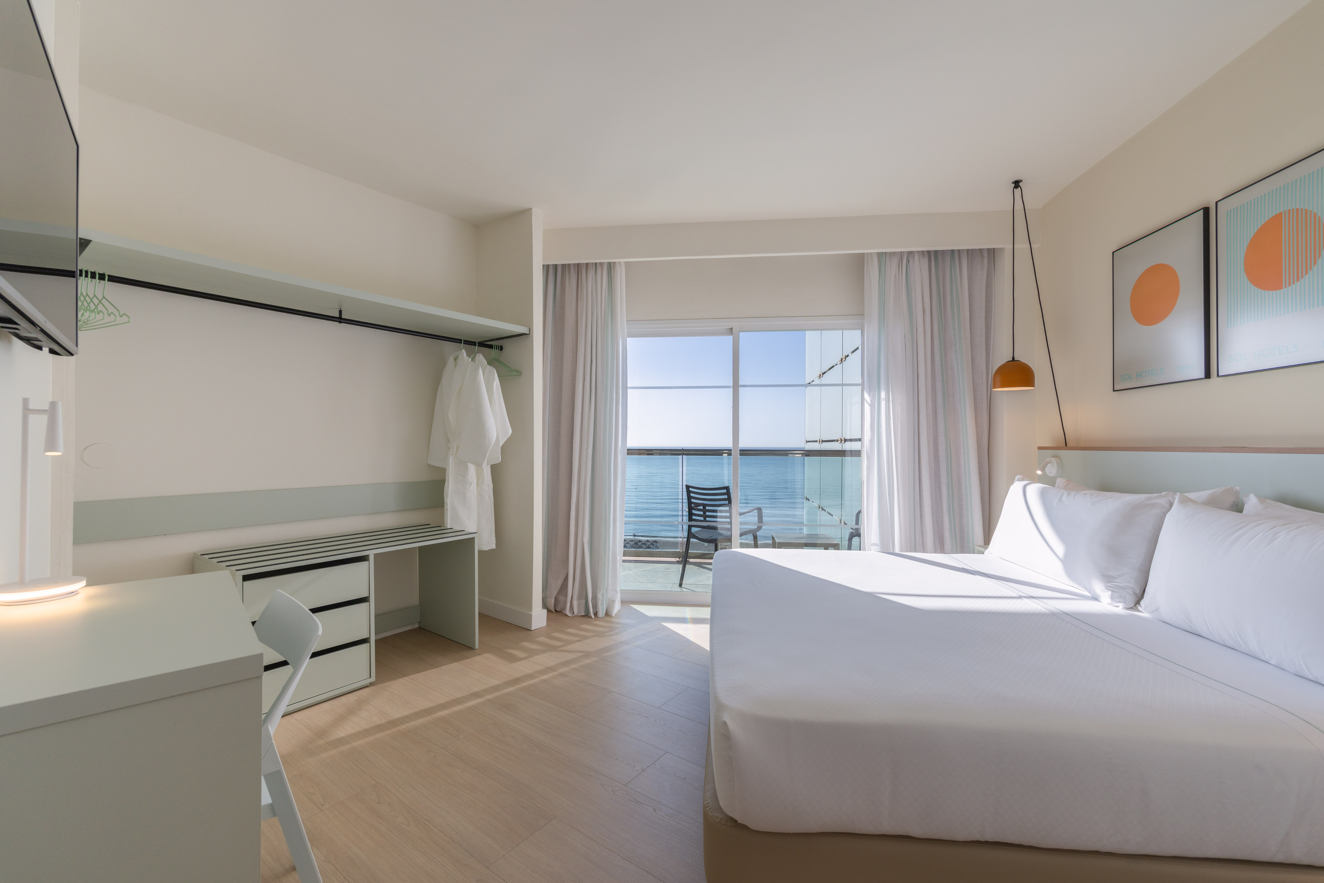 Bright hotel bedroom with sea view balcony, large bed, and modern desk.