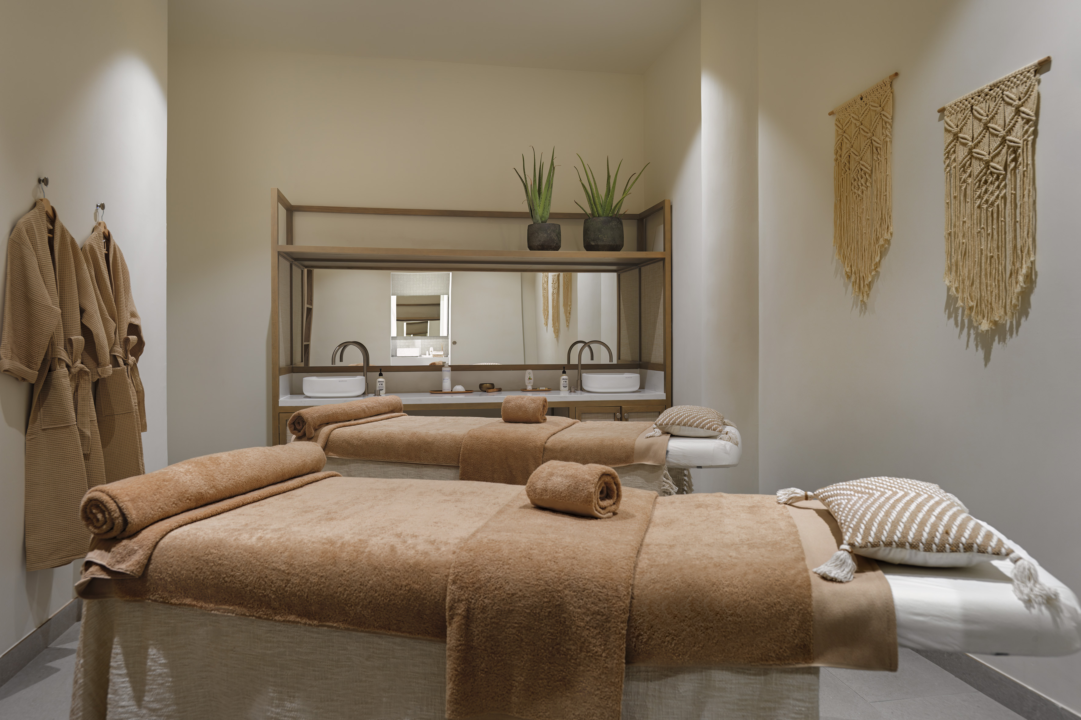 Serene spa room with two massage tables, robes, and neutral decor.