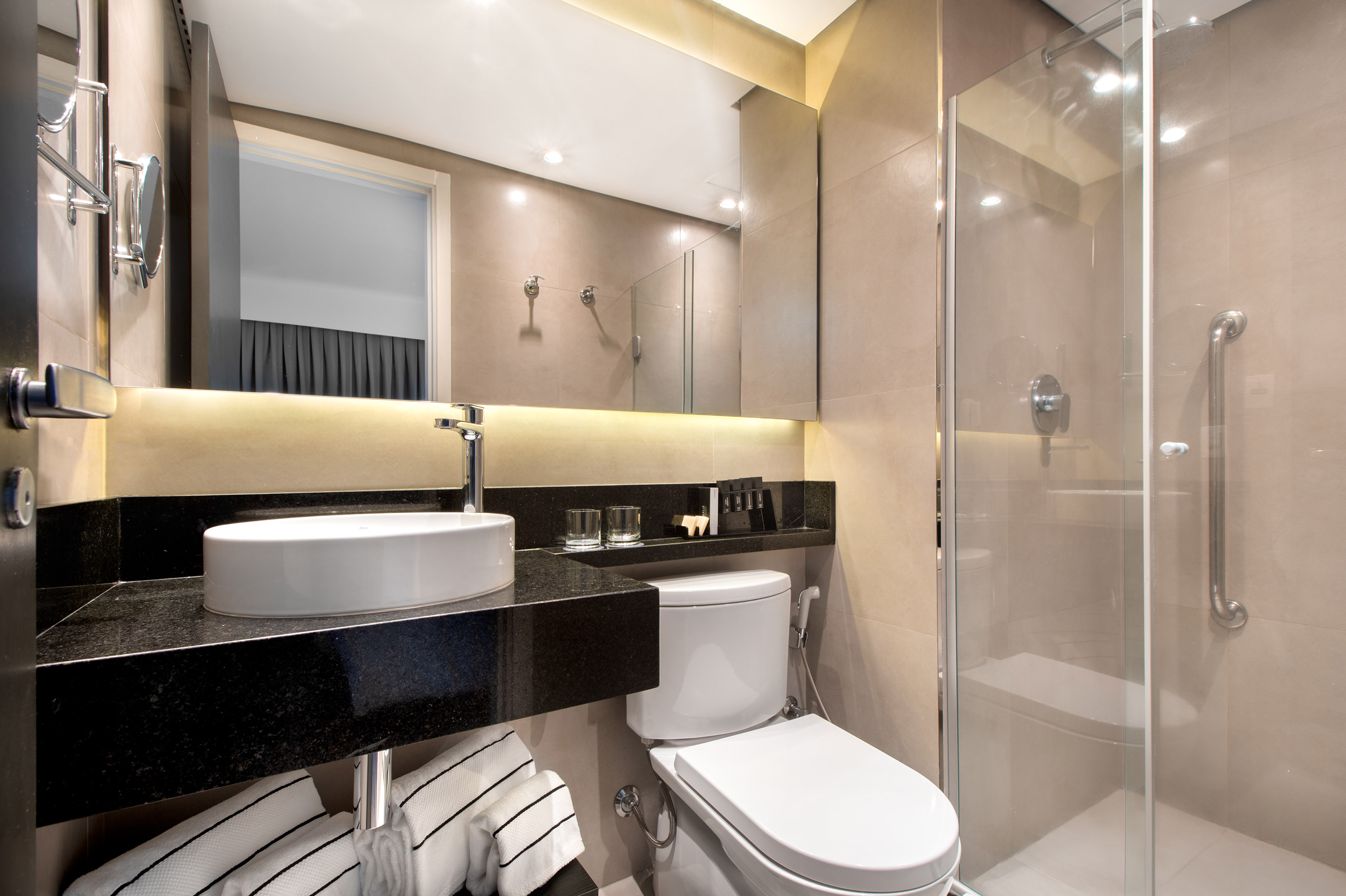 Modern hotel bathroom with vessel sink, black counter, toilet, and accessible glass shower.