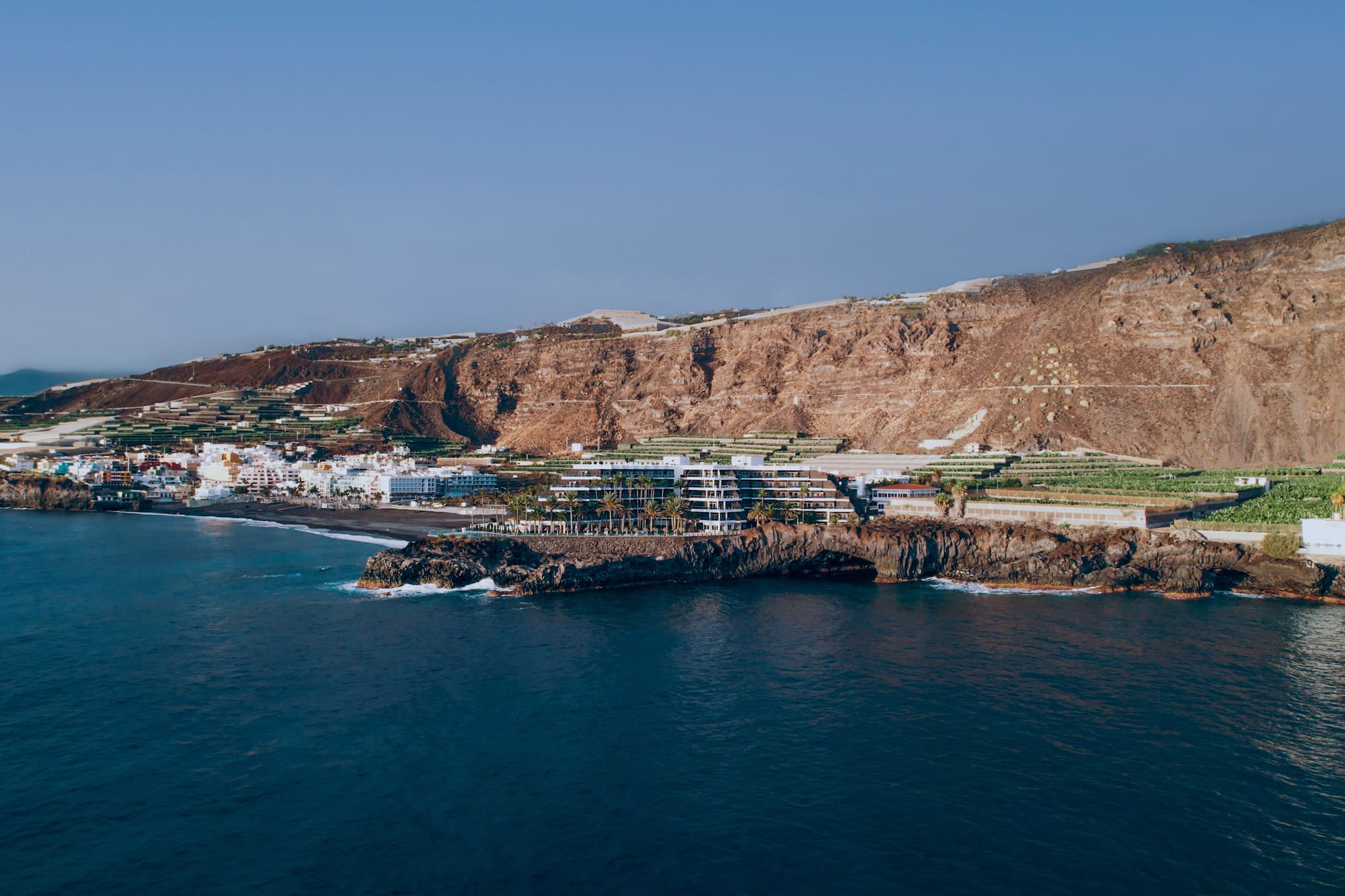Coastal town on black sand beach with resort, terraced farms, and ocean