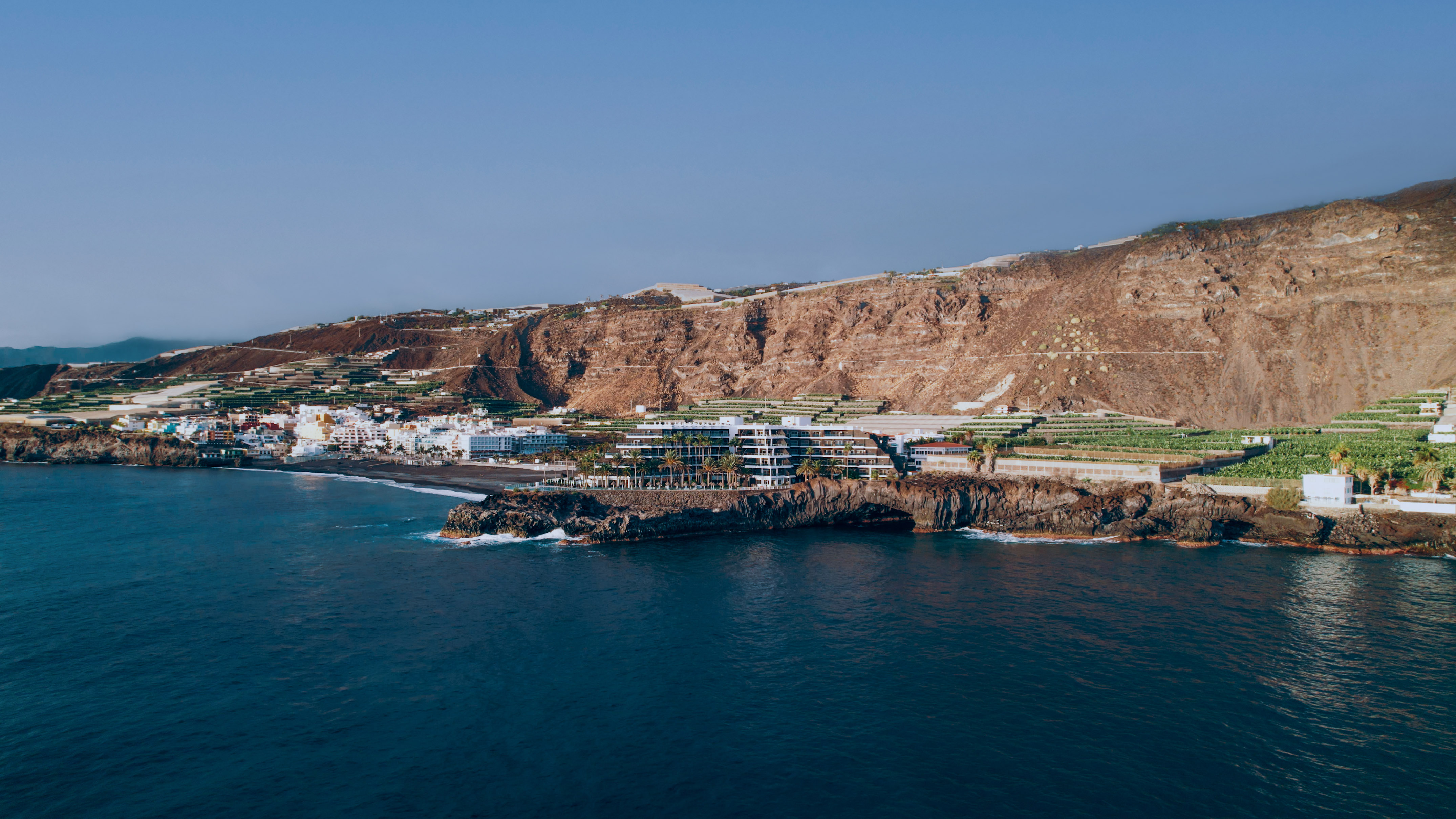 Coastal town on black sand beach with resort, terraced farms, and ocean