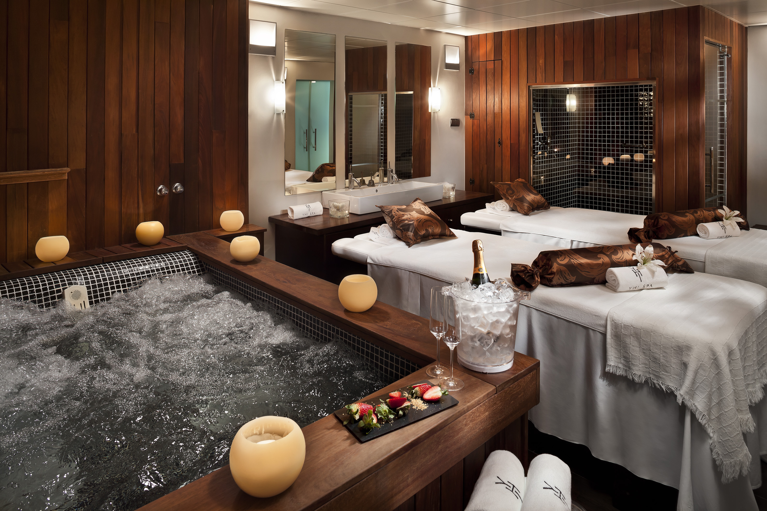 Luxury spa room with jacuzzi, massage beds, champagne, and strawberries.