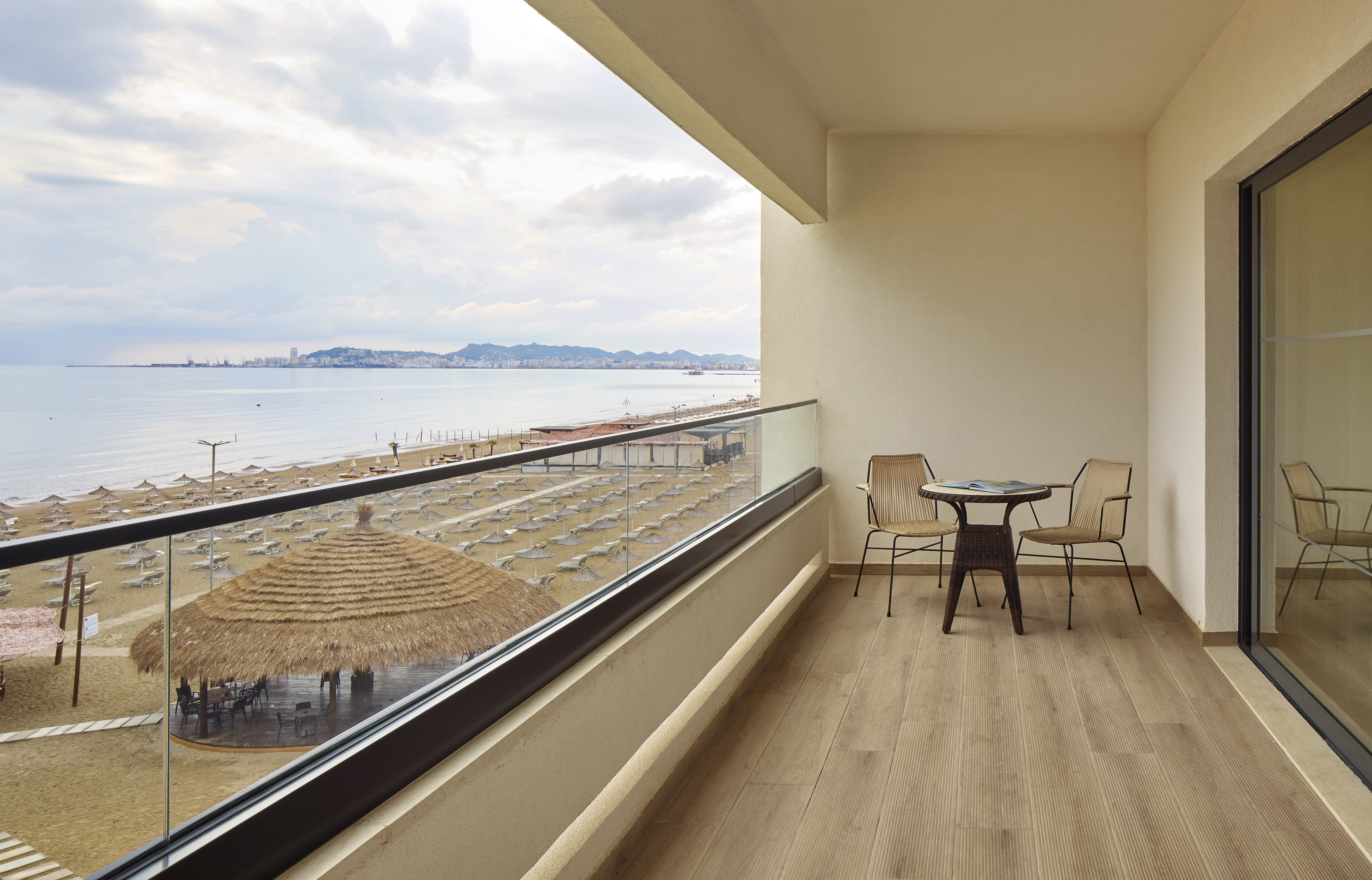 Balcony with sea view, sandy beach, sun loungers, and distant city.