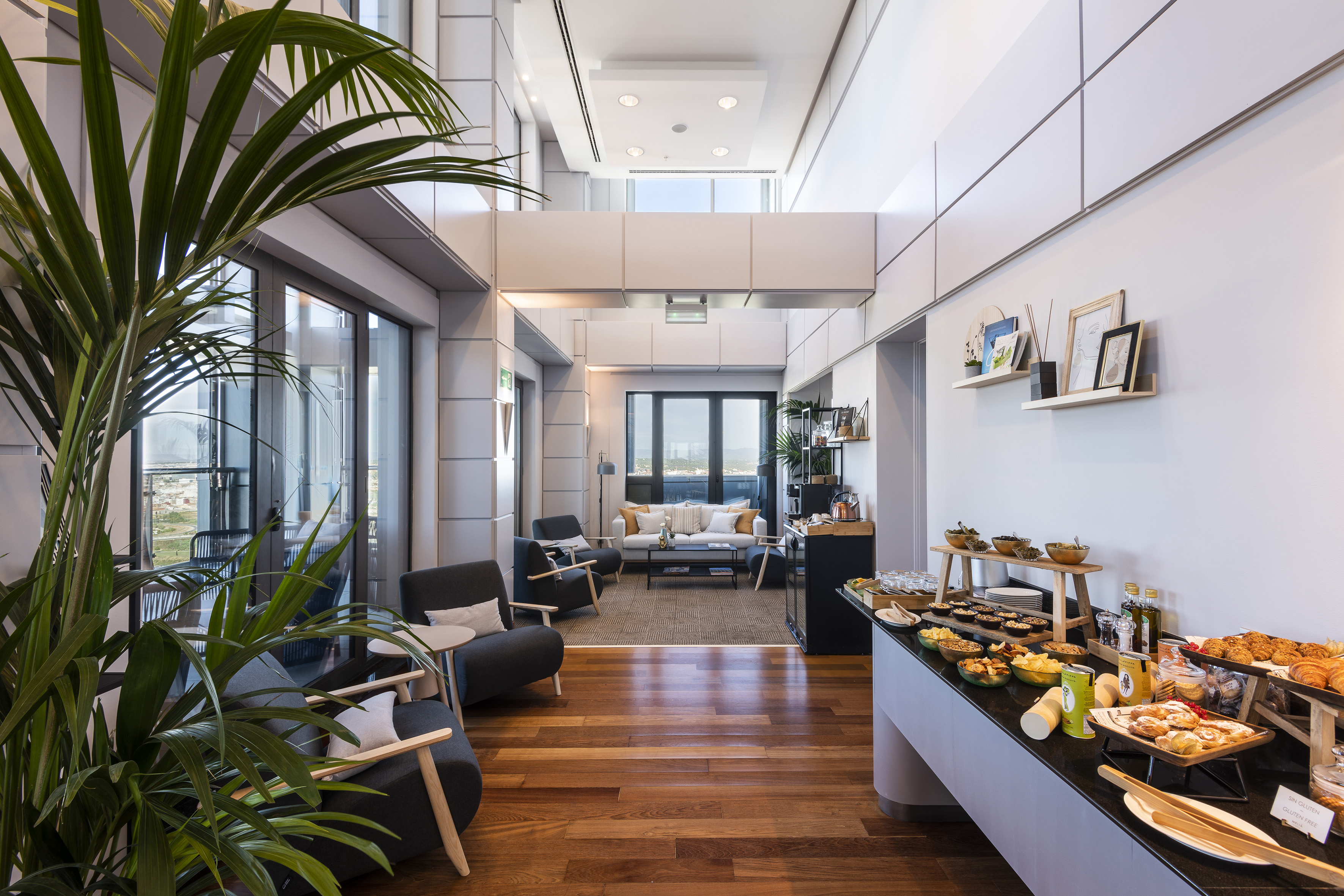 Modern lounge with buffet of pastries, snacks, comfortable seating, and city view.