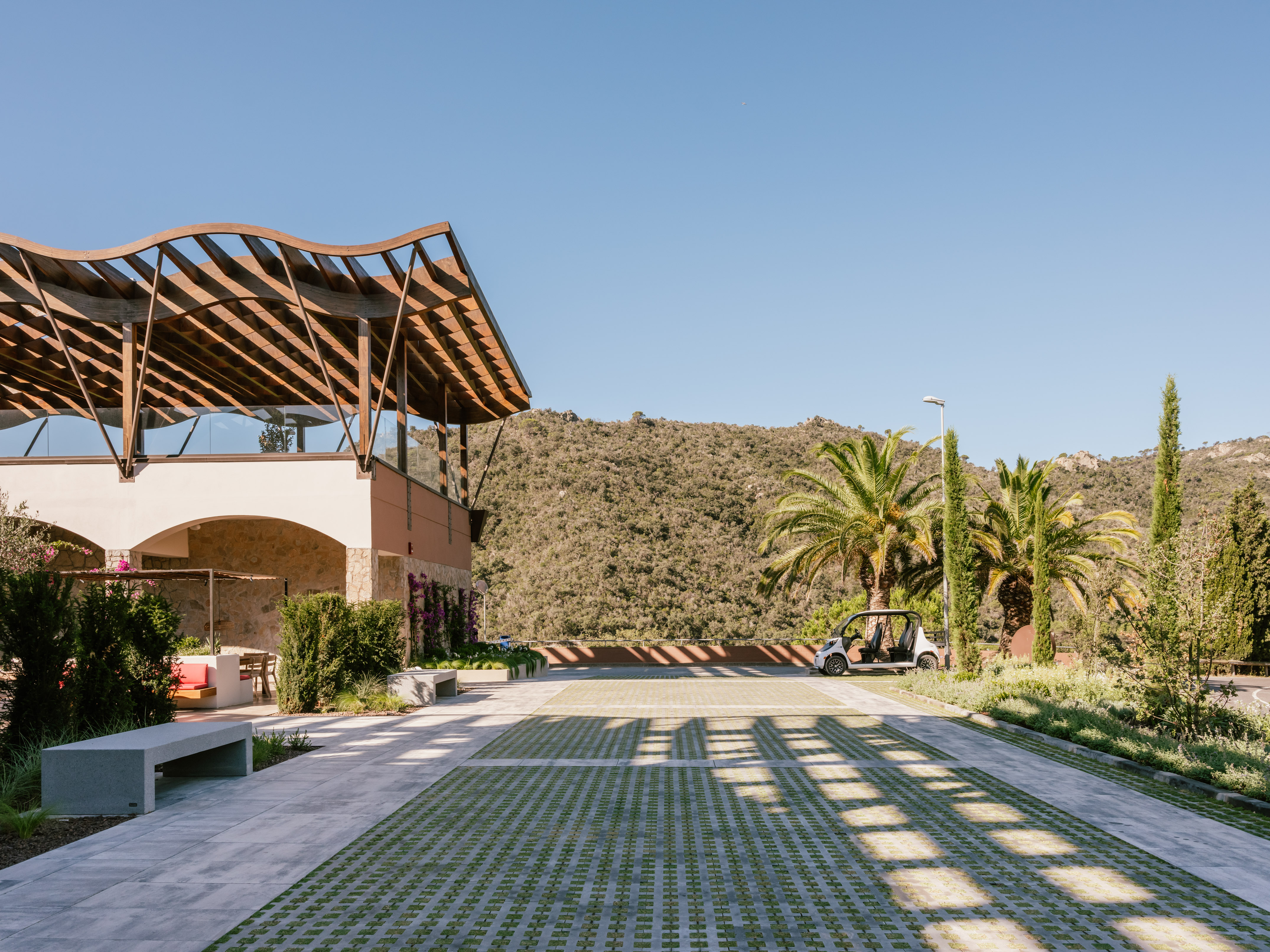 Modern building with wooden pergola, green grid parking, sunny landscape.