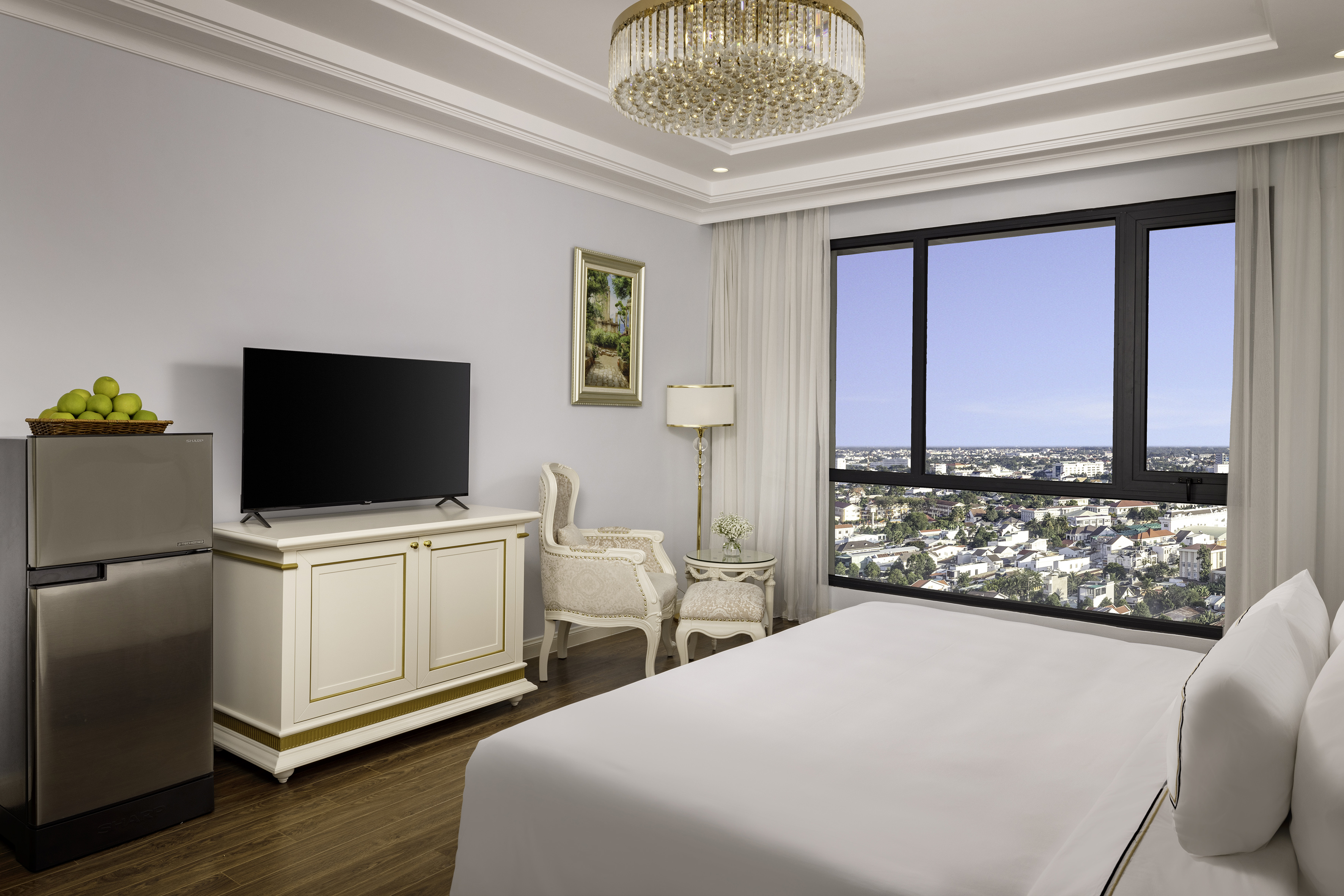 Luxury hotel room with city view, bed, TV, mini-fridge, and chandelier.