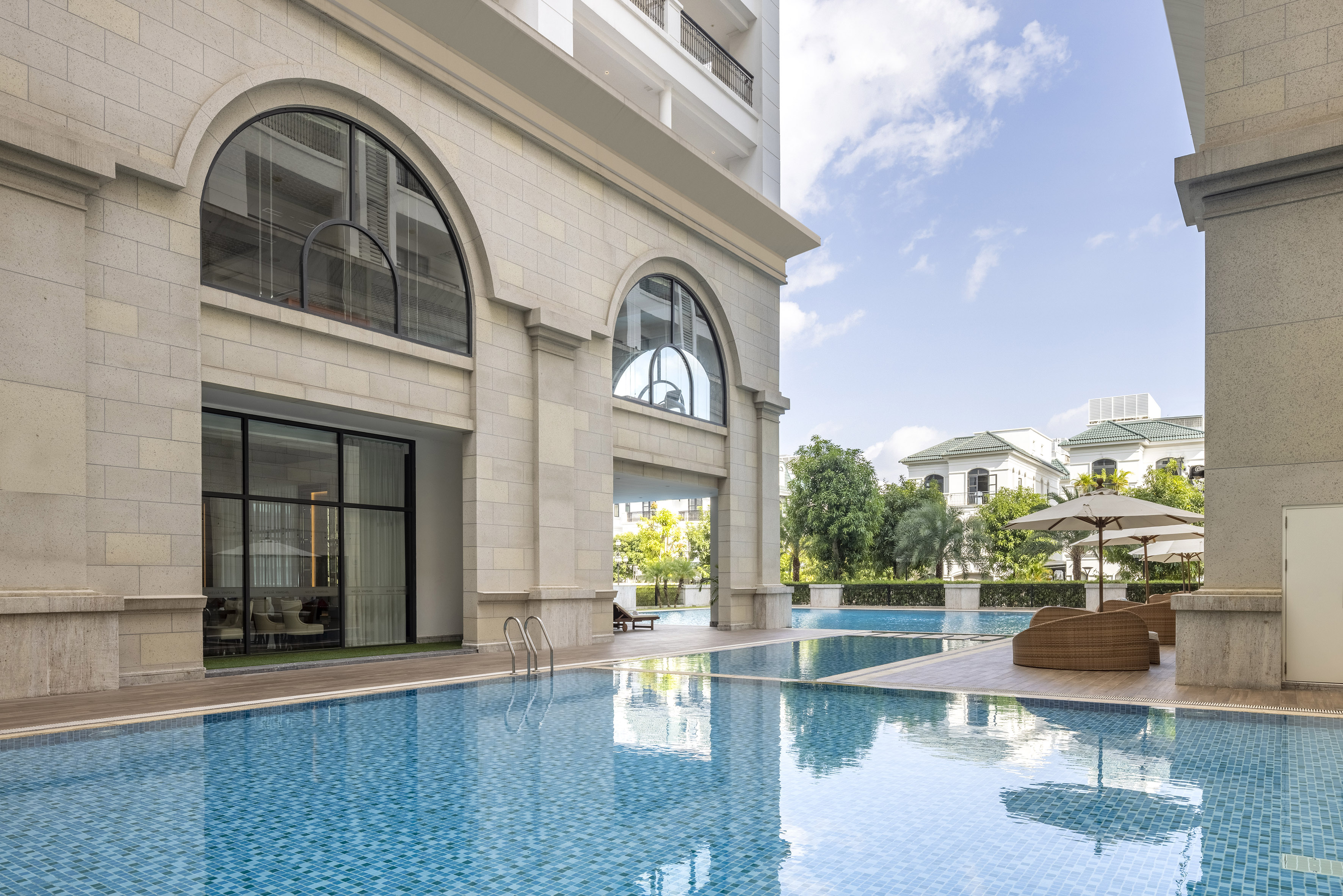 Outdoor swimming pool by a modern building with stone facade and arched windows.