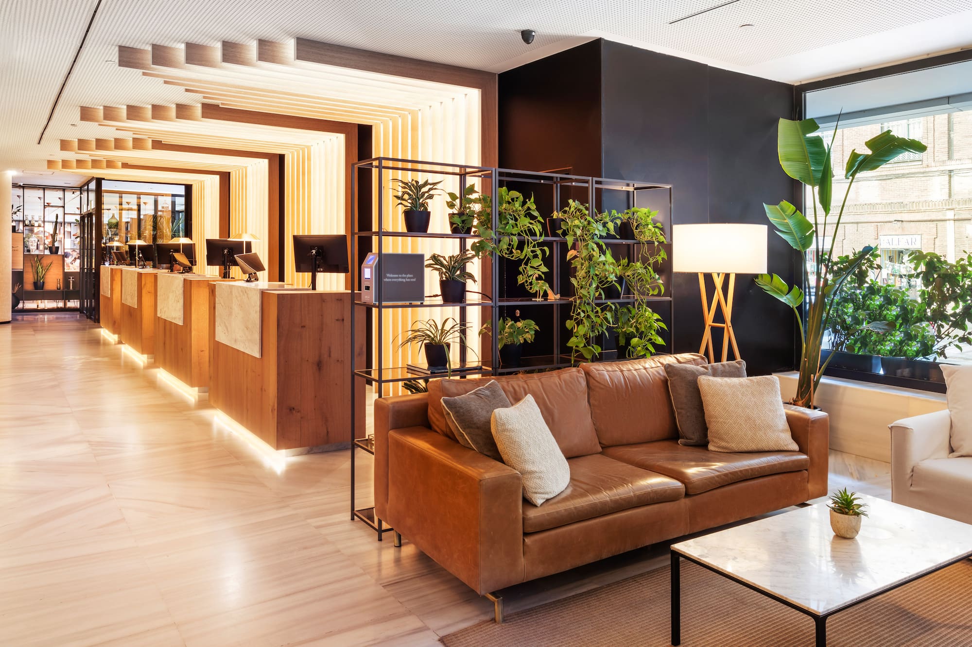 Contemporary hotel lobby featuring a wooden reception, leather sofa, and vibrant plants.