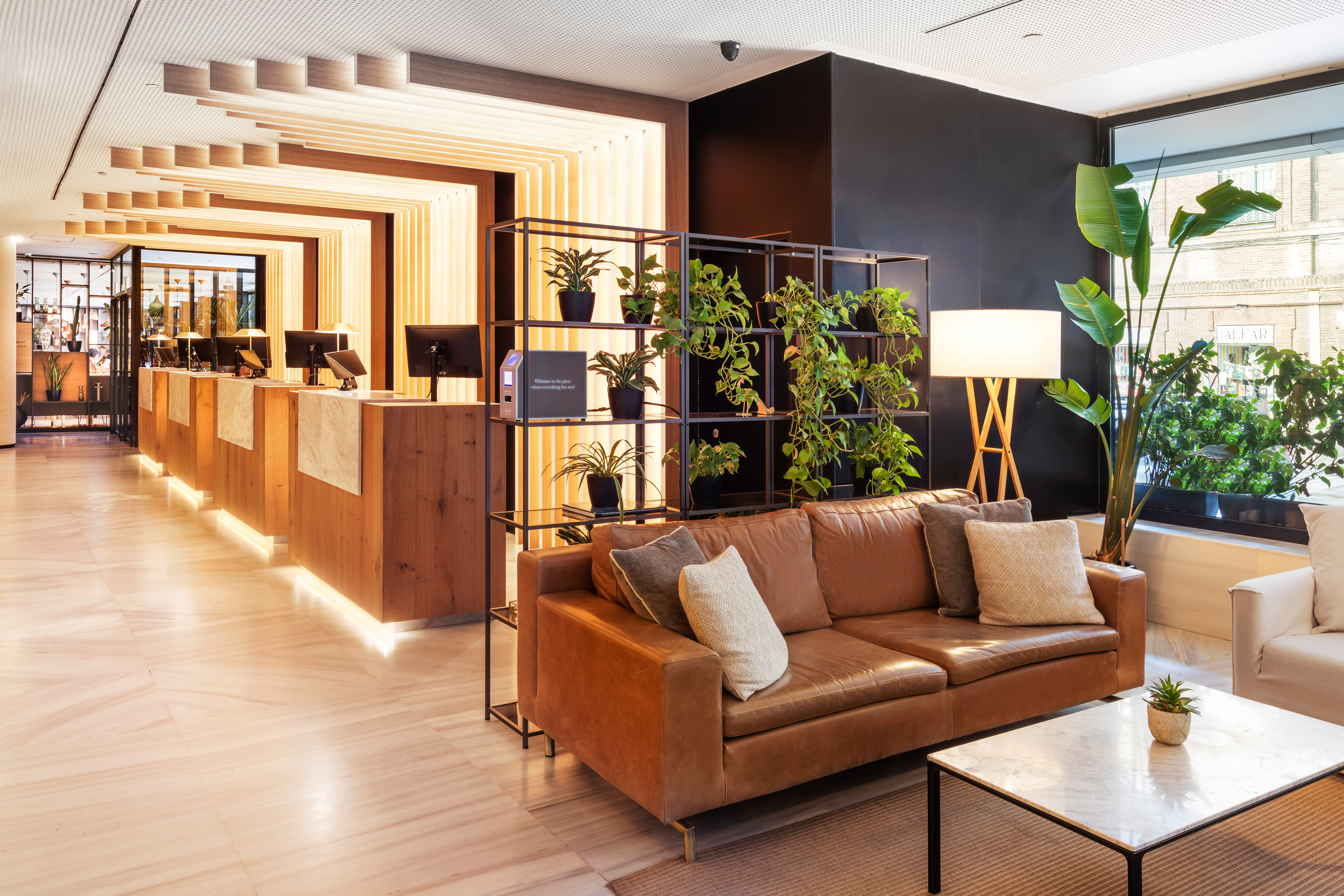 Contemporary hotel lobby featuring a wooden reception, leather sofa, and vibrant plants.