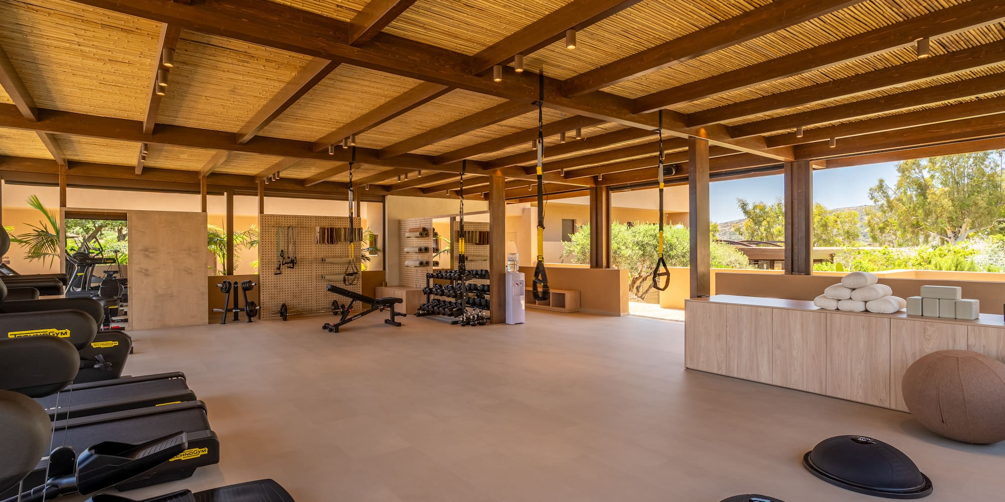 Resort gym with Technogym equipment, free weights, TRX, and bamboo ceiling.