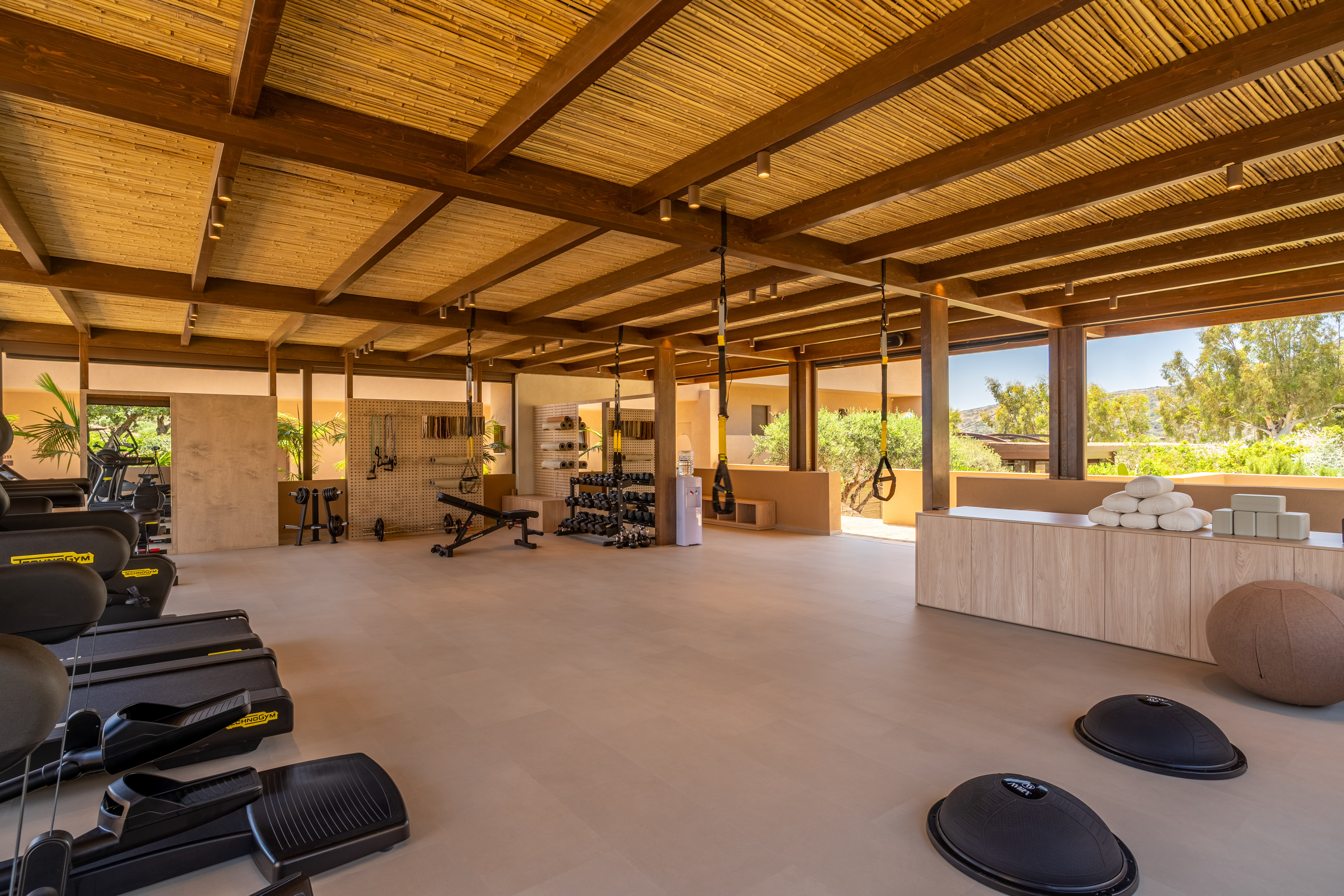 Resort gym with Technogym equipment, free weights, TRX, and bamboo ceiling.