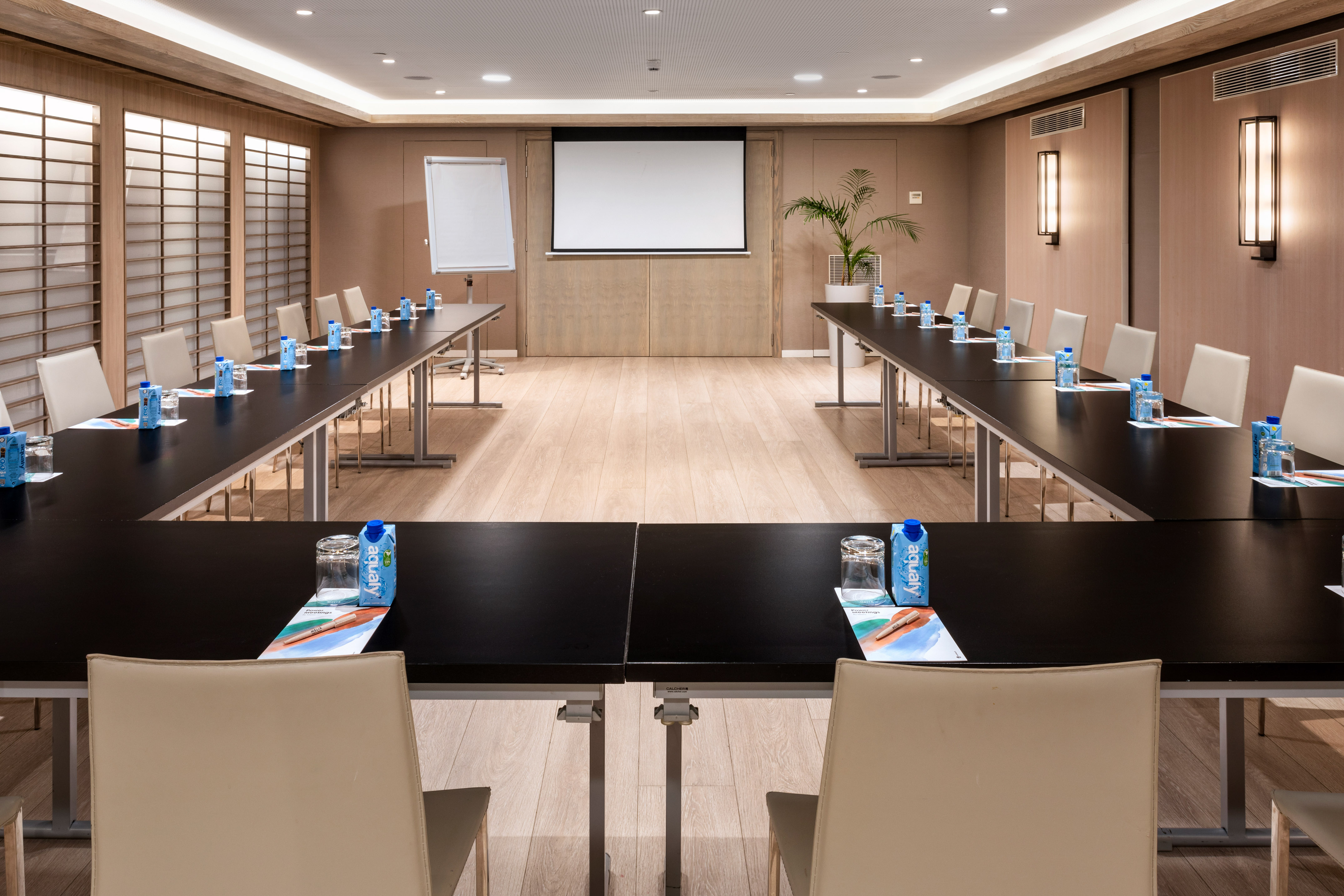 U-shaped meeting room with projector screen, whiteboard, and individual water bottles.