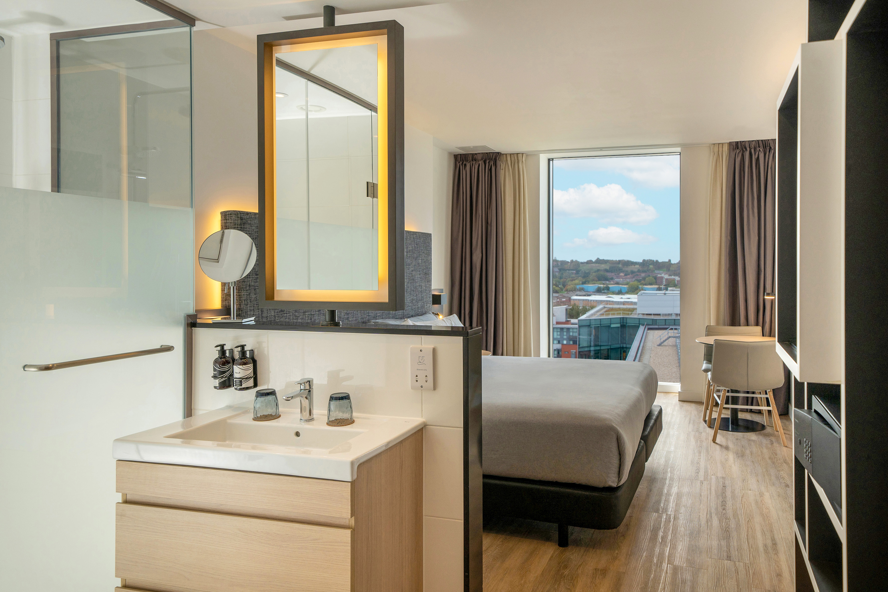 Modern hotel room with bed, integrated vanity, and city view window.