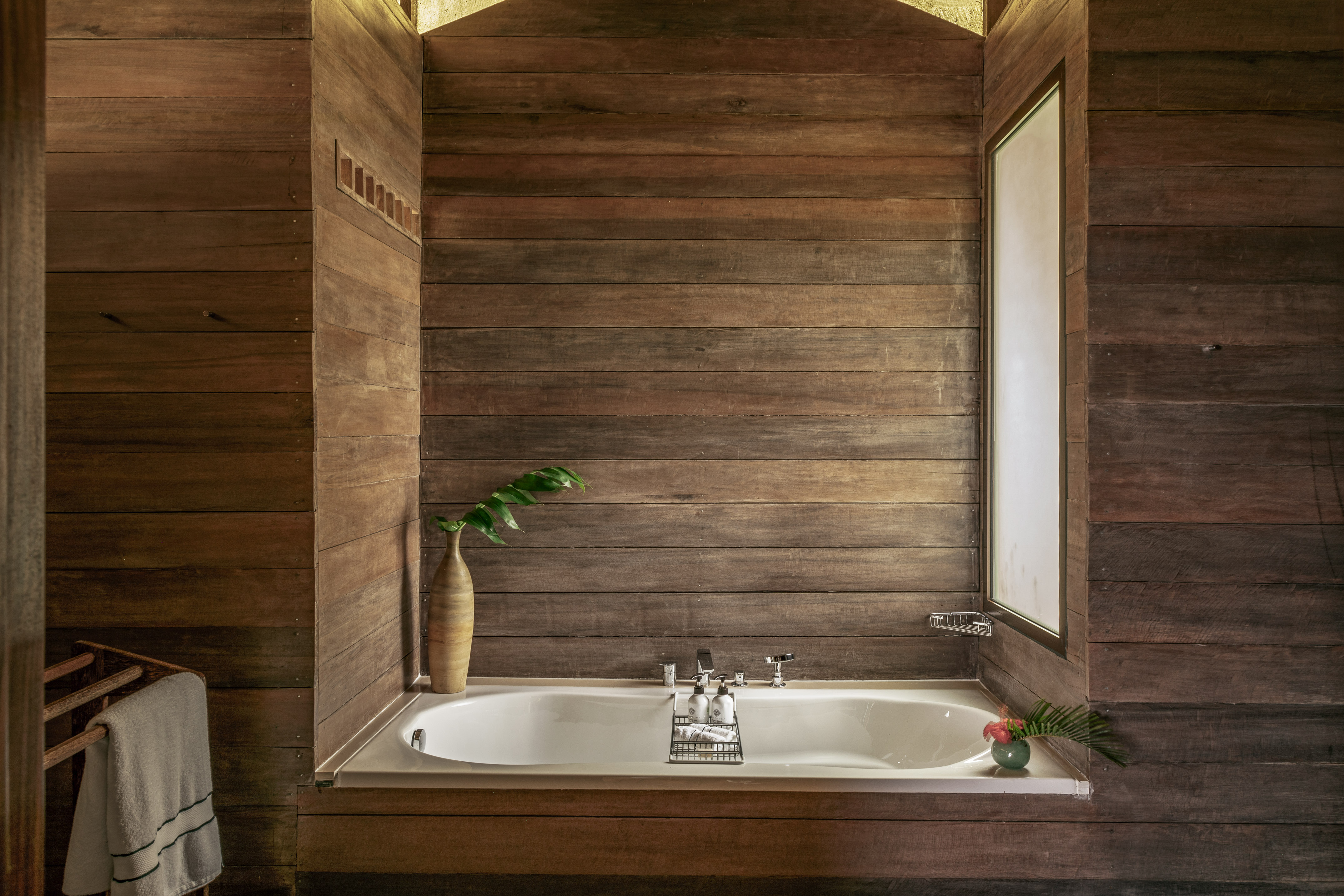 Rustic wooden bathroom with built-in tub, tropical decor, and natural light.