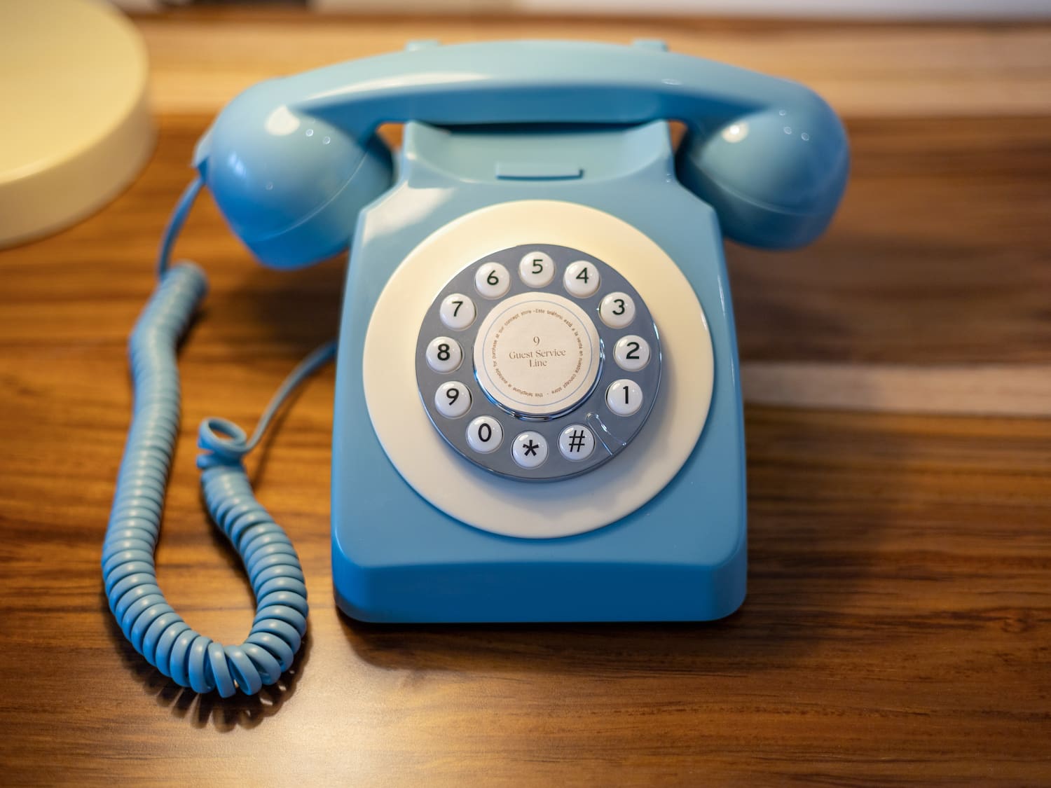 Light blue vintage rotary phone with 'Guest Service Line' dial on wood.