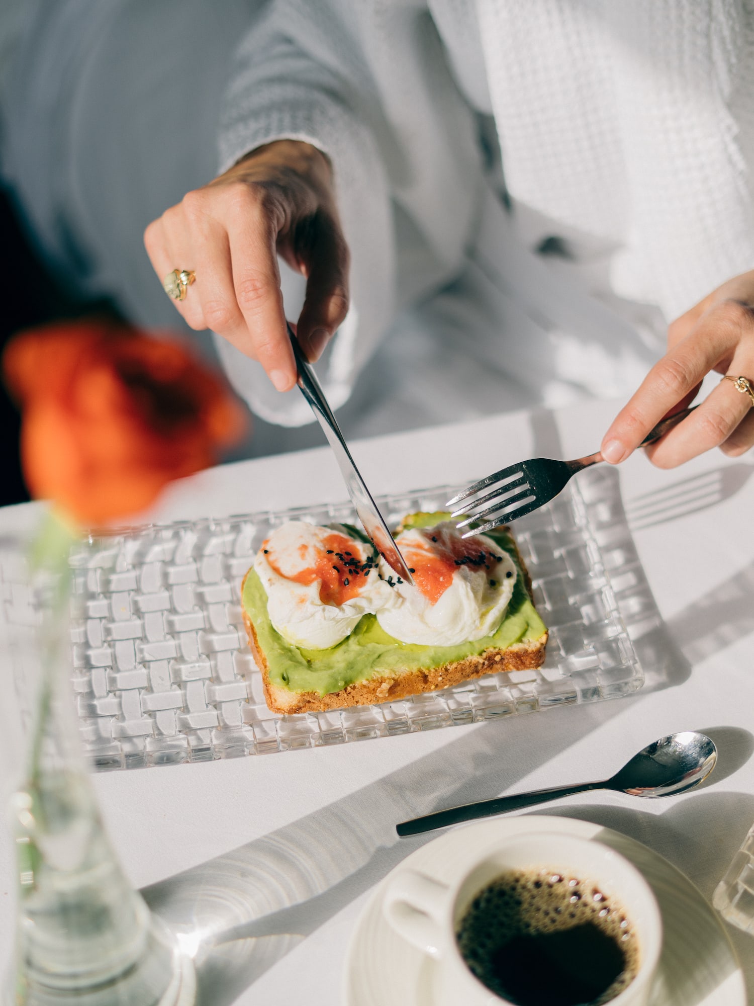 Hands cutting avocado toast with poached eggs, sauce, and coffee at a hotel breakfast.