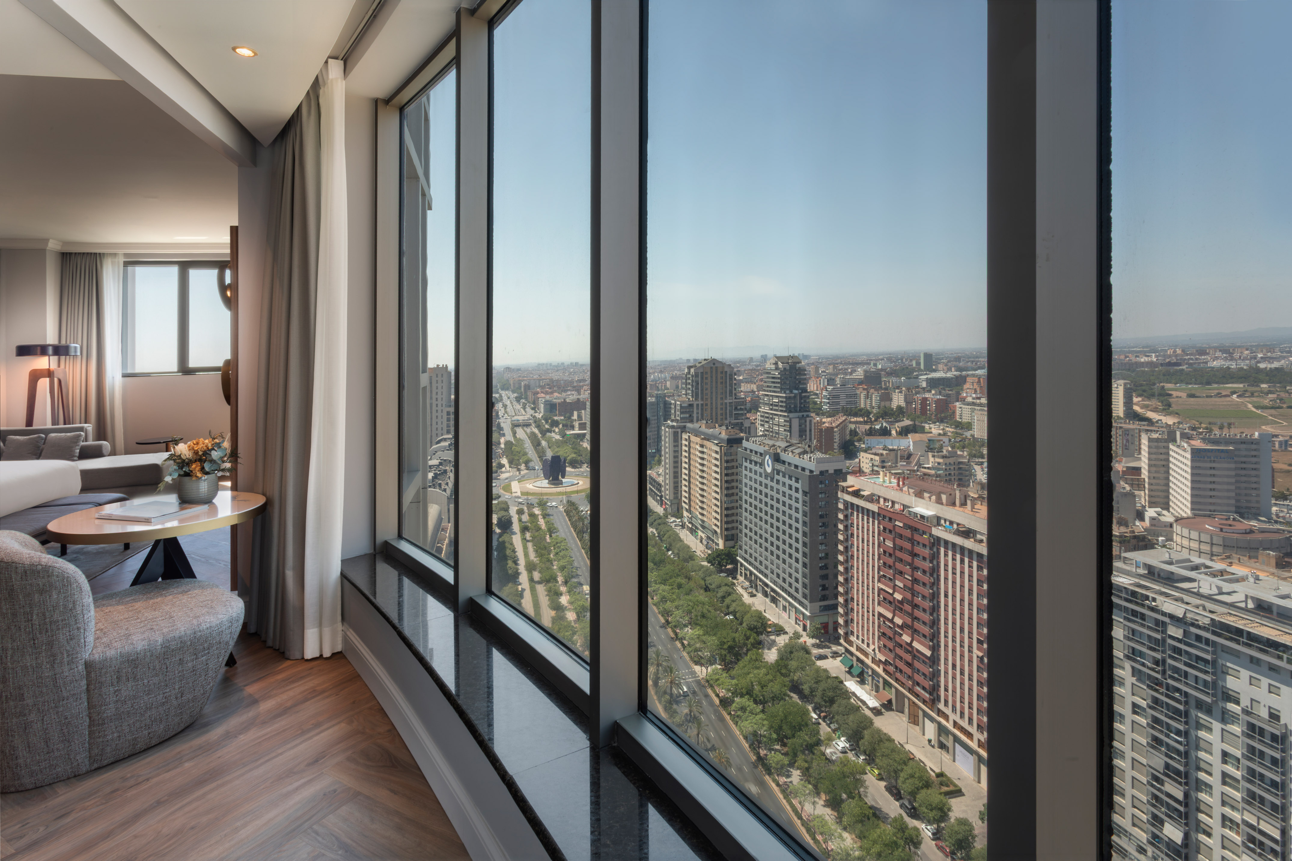 Moderna suite de hotel con vistas panorámicas a la ciudad y avenida arbolada.