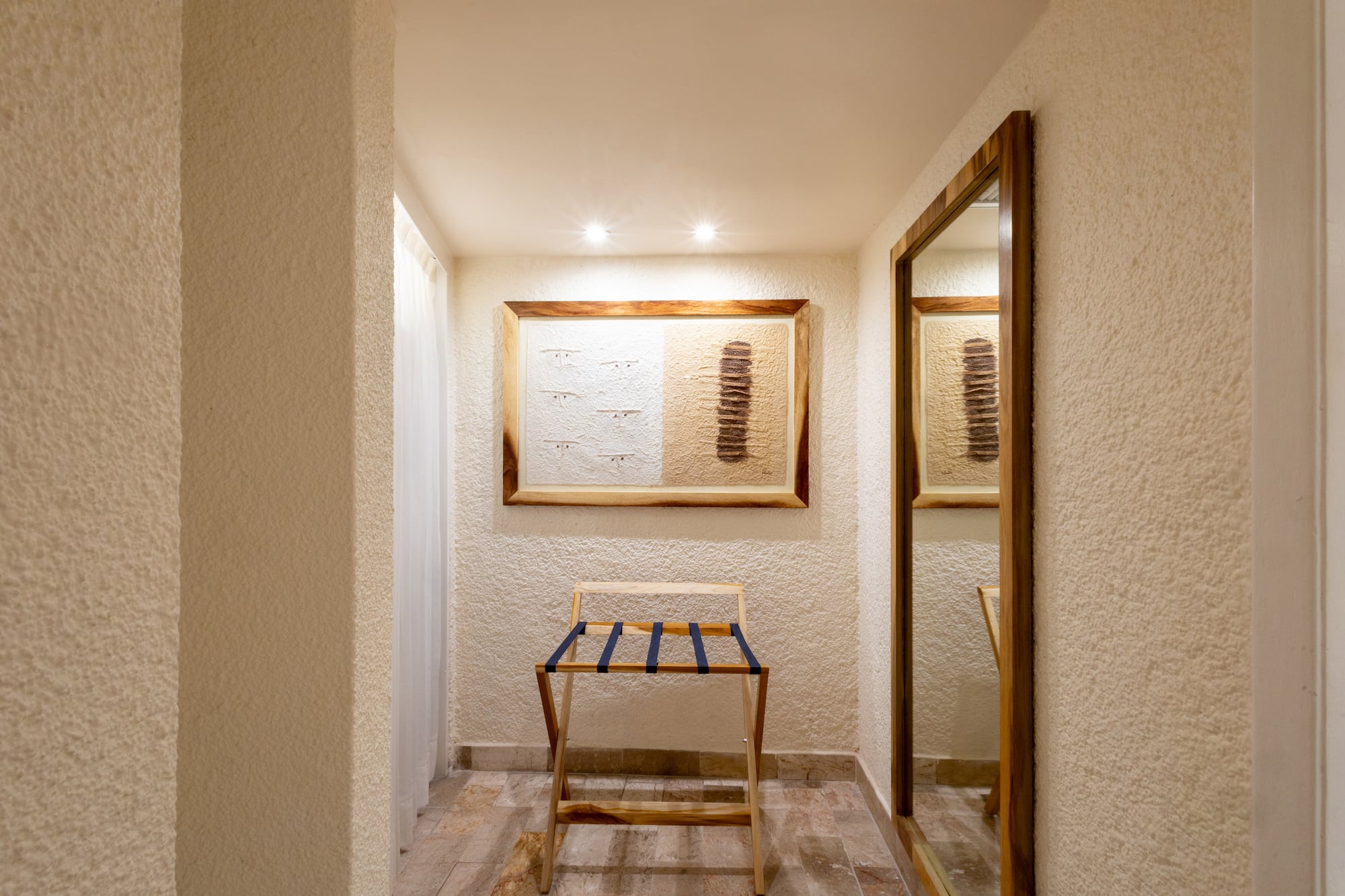 Hotel room entryway with wooden luggage rack, framed art, and full-length mirror.