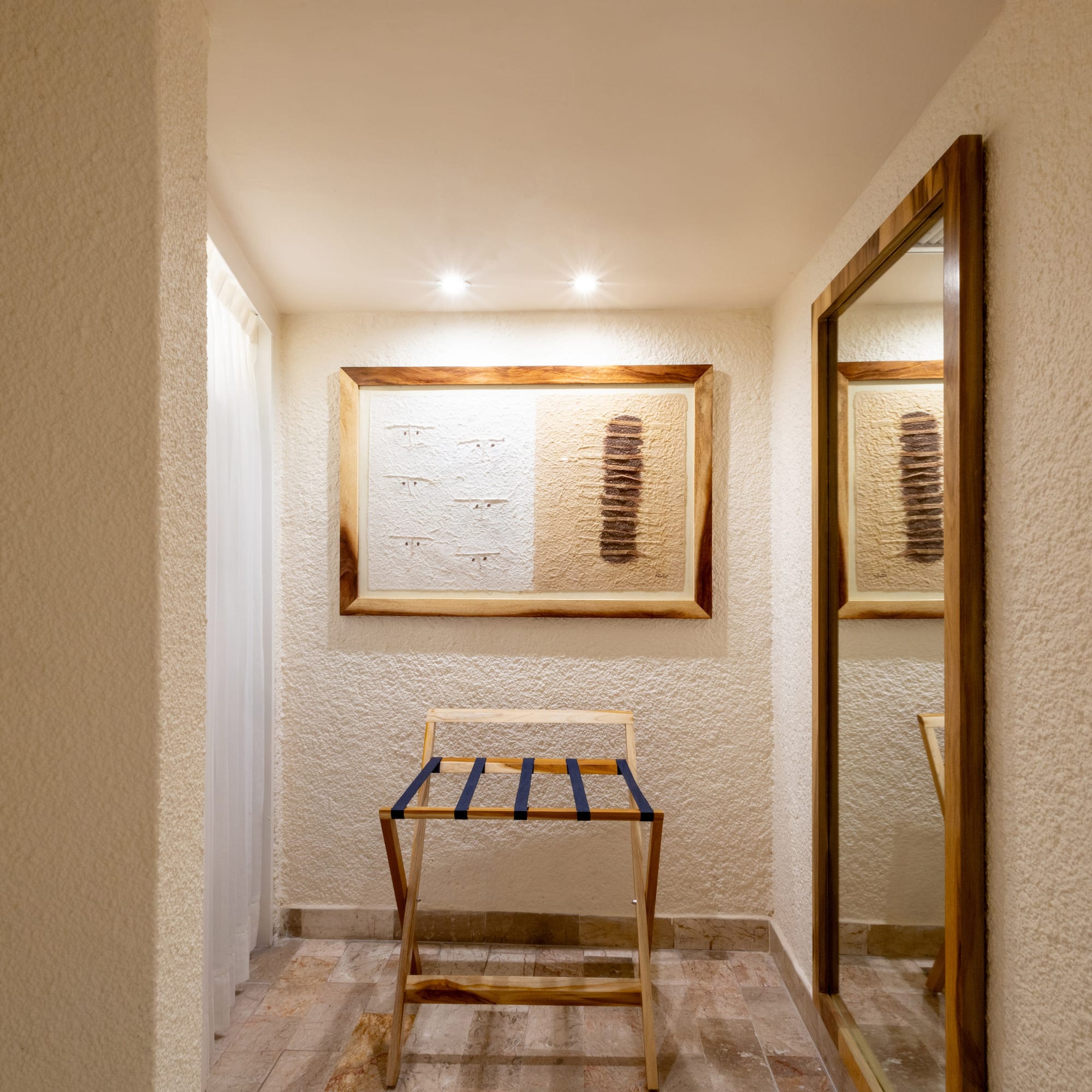 Hotel room entryway with wooden luggage rack, framed art, and full-length mirror.