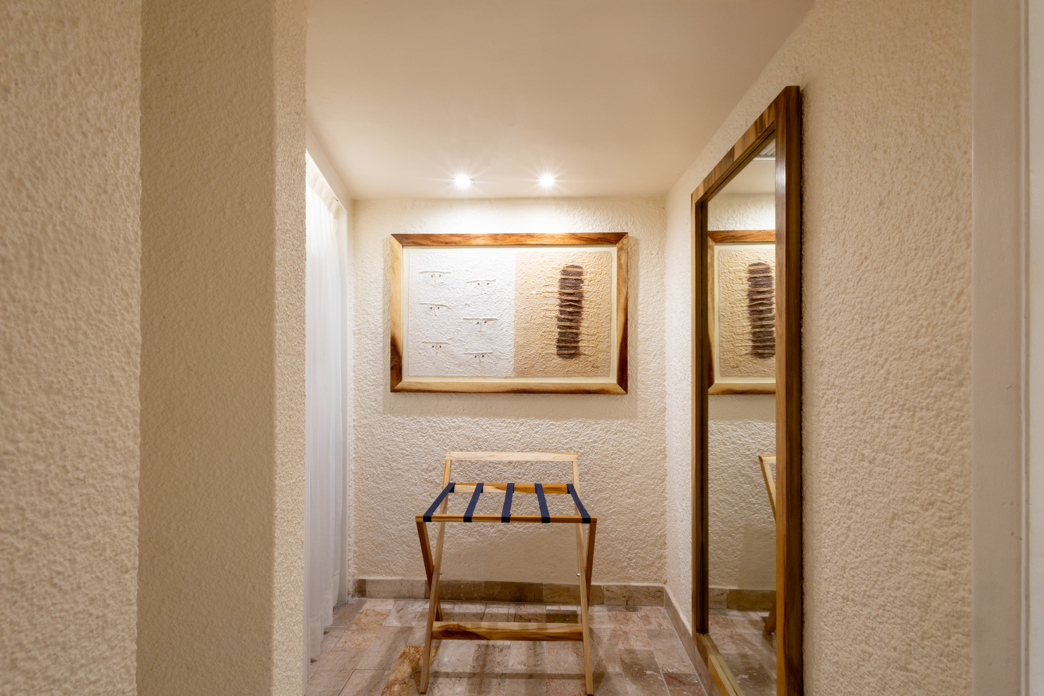 Hotel room entryway with wooden luggage rack, framed art, and full-length mirror.