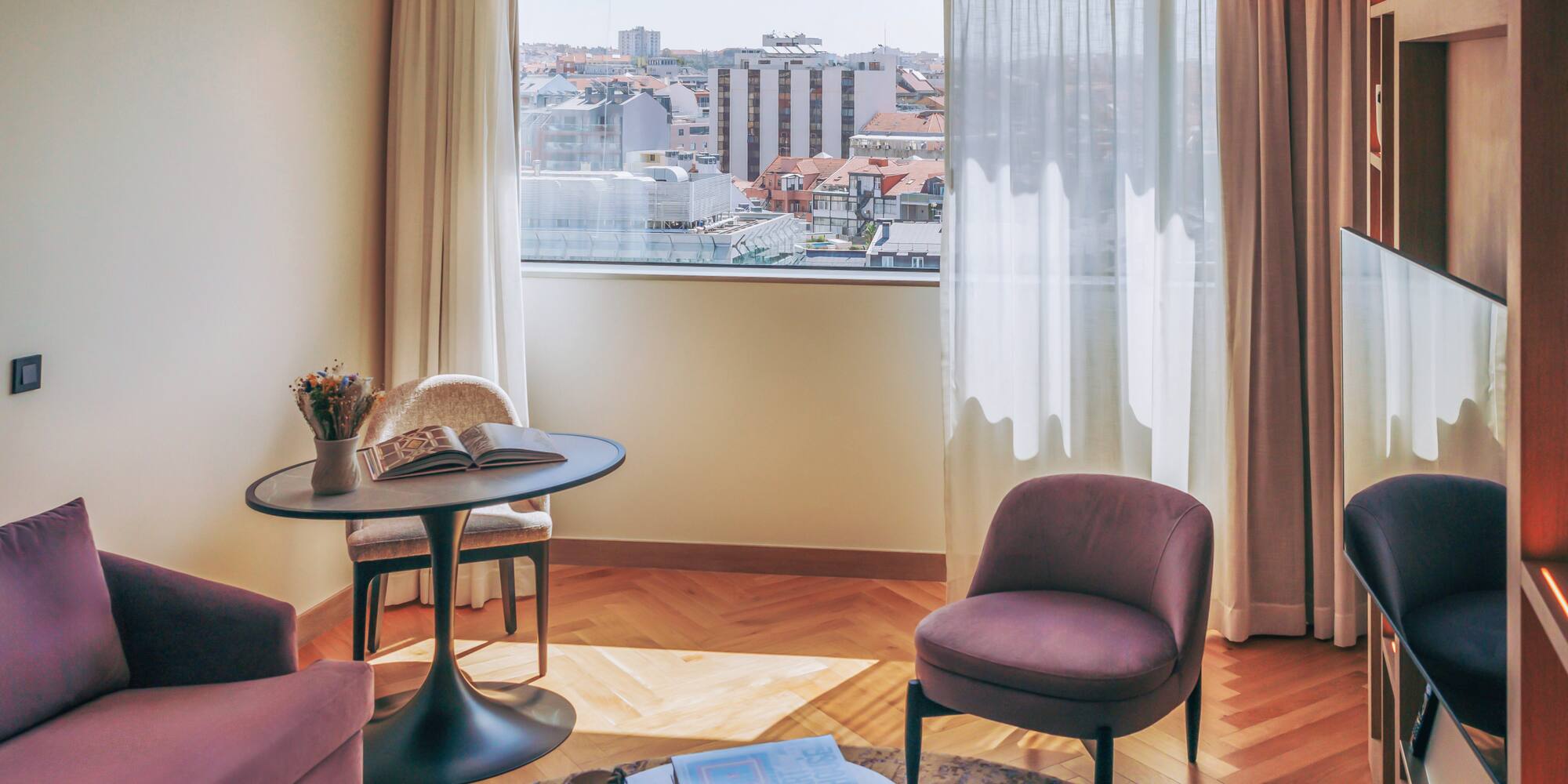 Hotel room lounge with city view, purple seating, and herringbone wood floor.