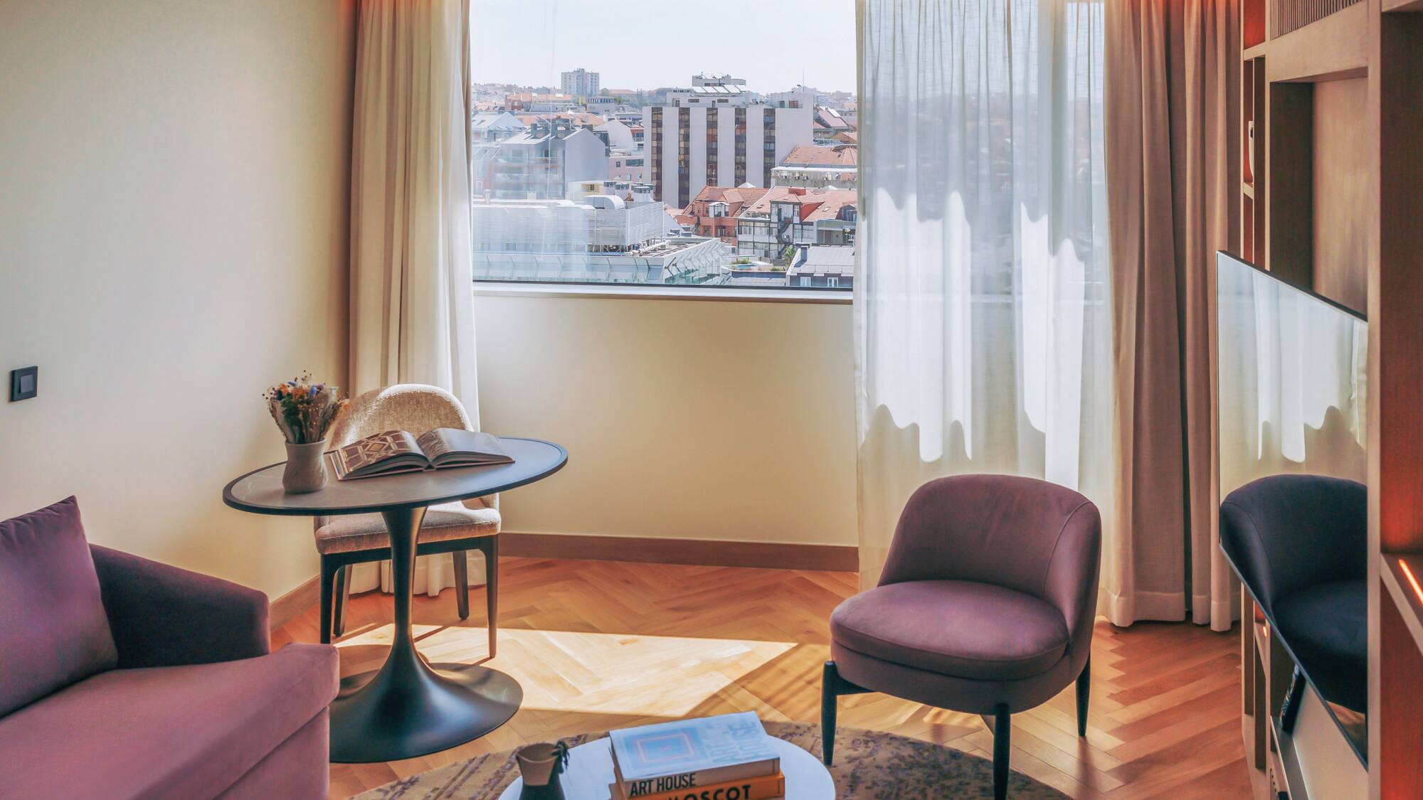 Hotel room lounge with city view, purple seating, and herringbone wood floor.
