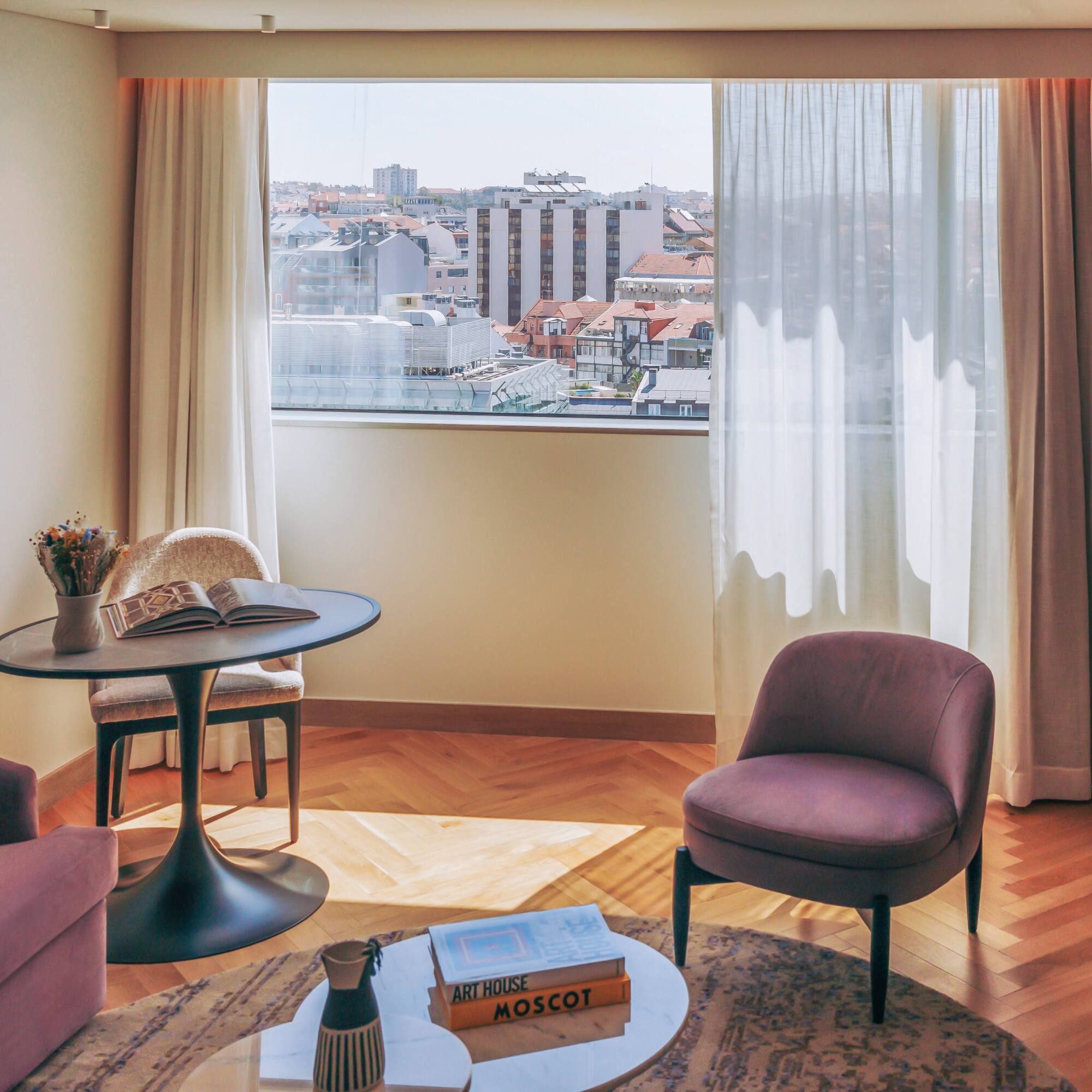 Hotel room lounge with city view, purple seating, and herringbone wood floor.