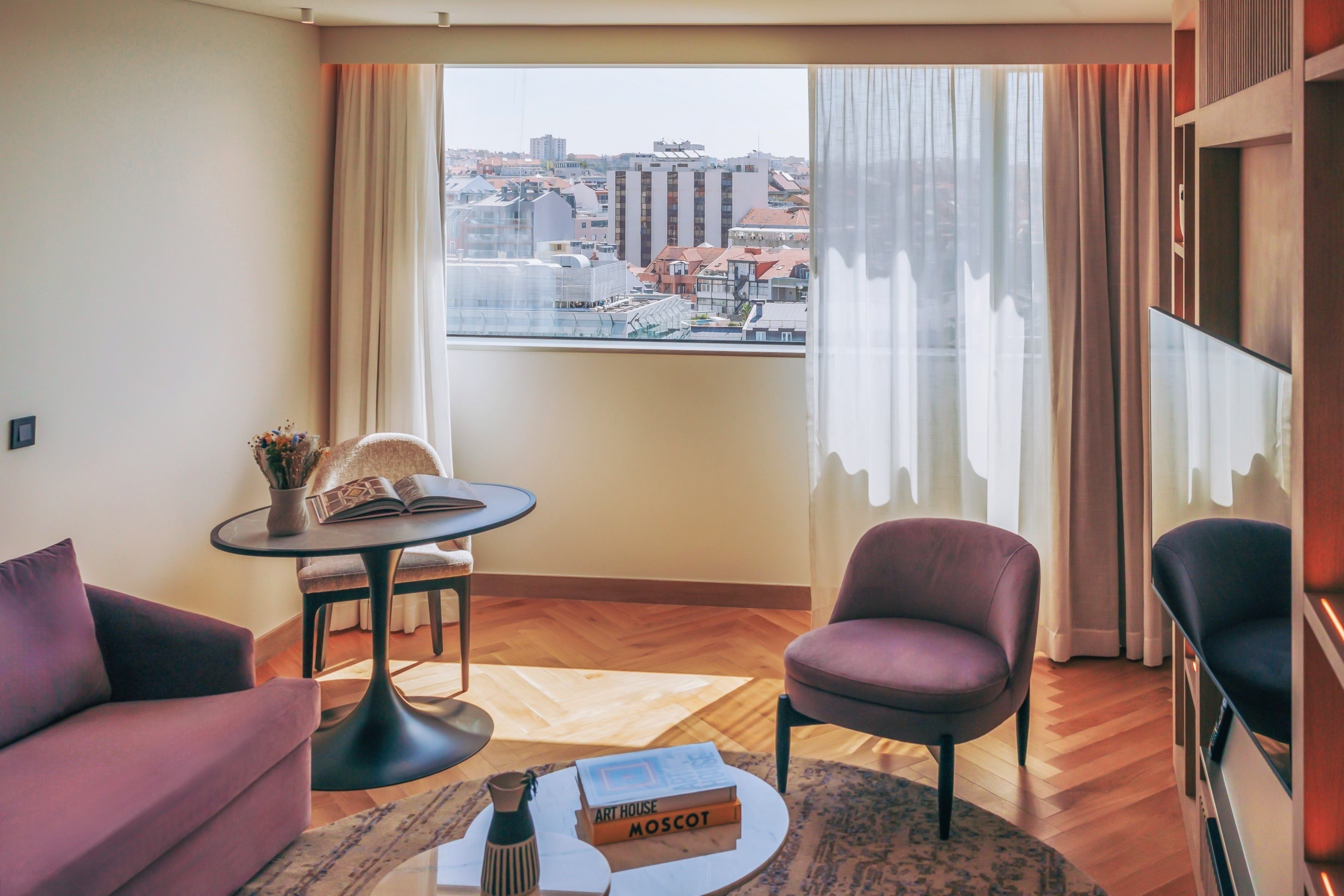 Hotel room lounge with city view, purple seating, and herringbone wood floor.