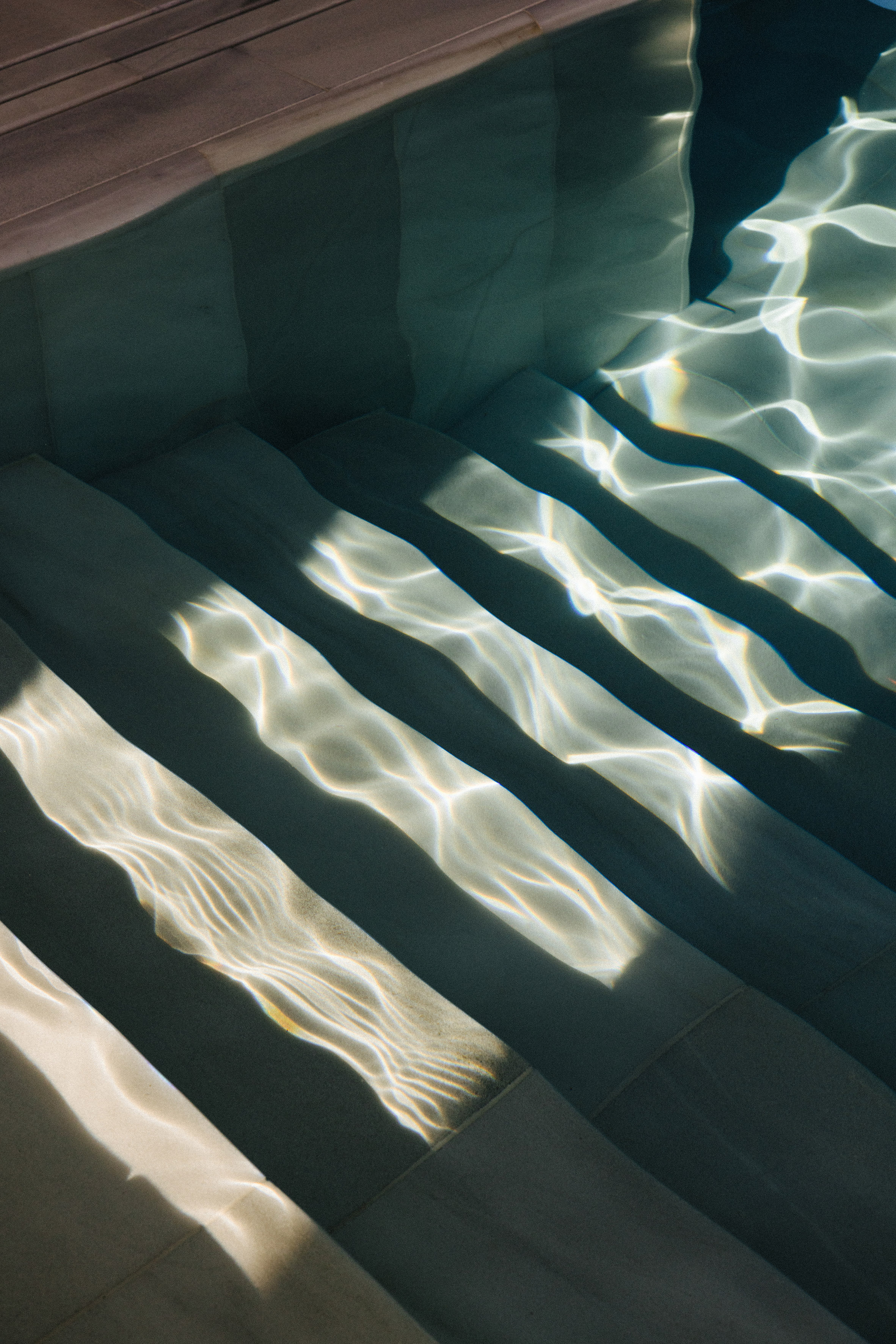 Underwater pool steps with shimmering sunlight patterns.