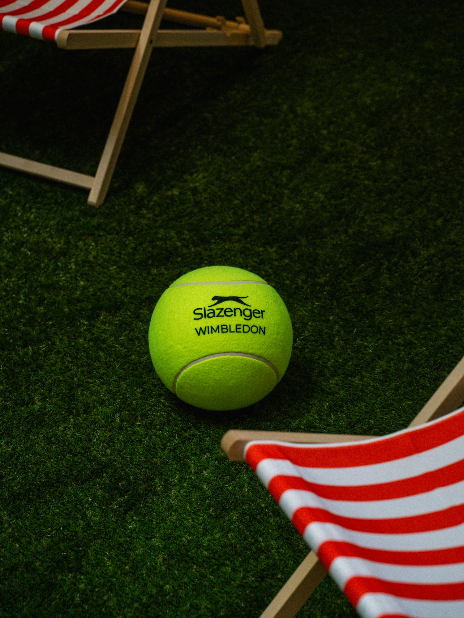 Slazenger Wimbledon tennis ball on a green grass court with striped deck chairs.