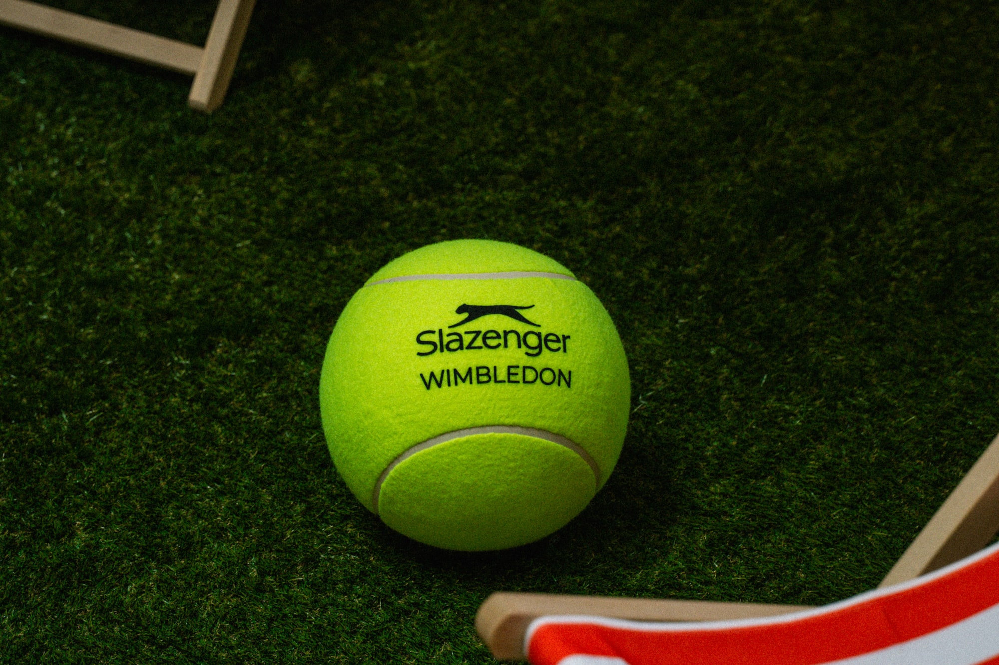 Slazenger Wimbledon tennis ball on a green grass court with striped deck chairs.