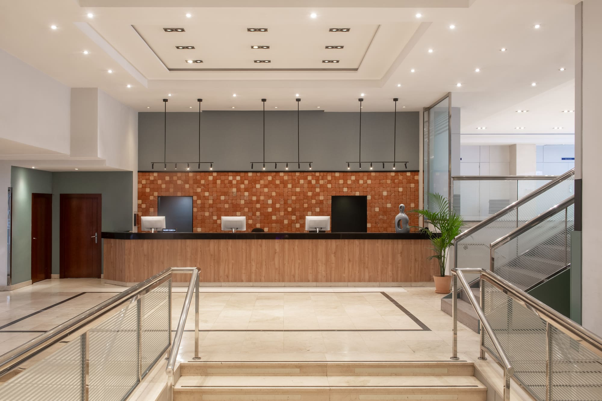 Modern hotel lobby with reception desk, brick accent wall, and elegant staircase.
